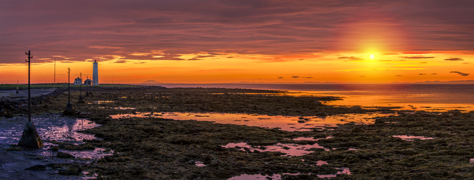 Low midnight sun over the tidal shore and lighthouse at Grótta