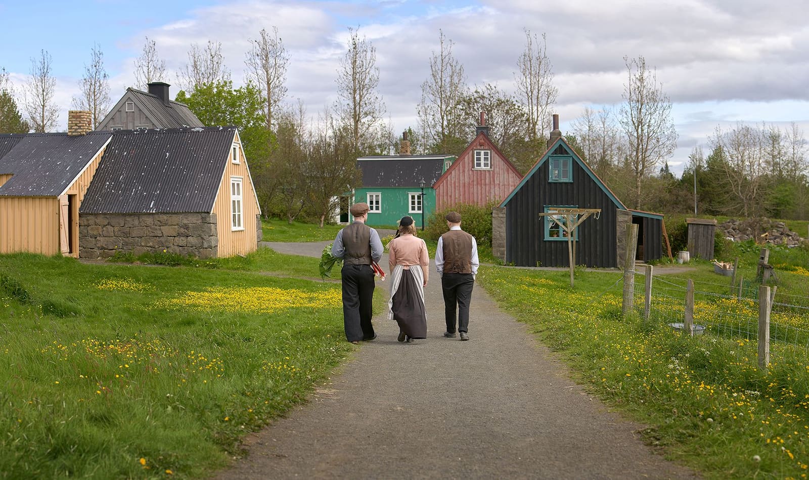 Costumed interpreters walking between historic buildings at Árbær Open Air Museum