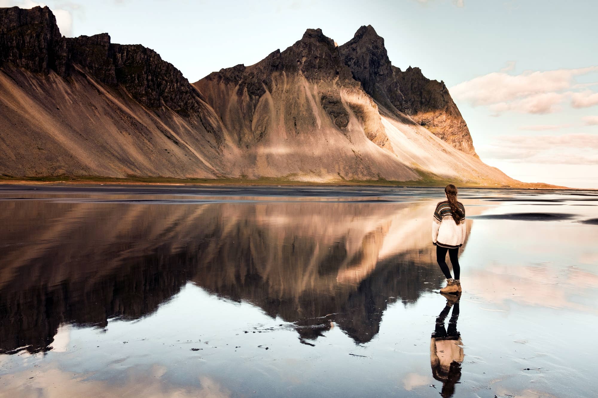 Vestrahorn mountain reflected in wet sand beside a traveler at Stokksnes