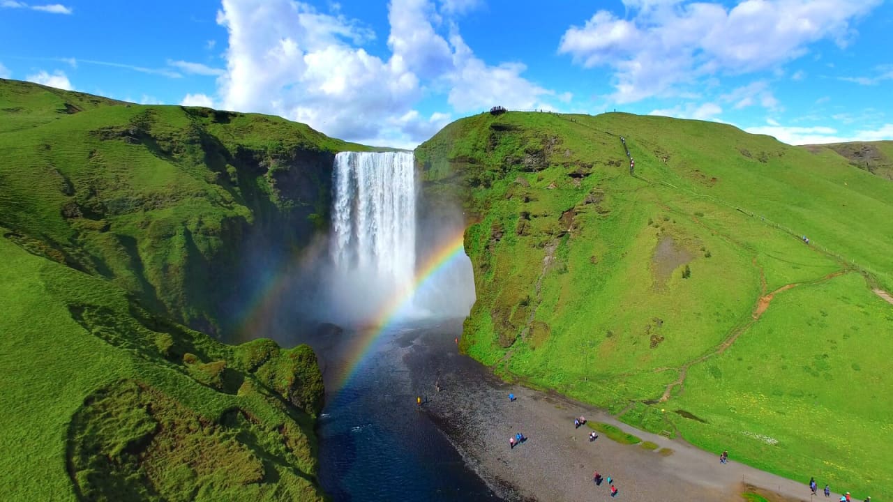 Skogafoss waterfall and rainbow mist below green South Iceland cliffs