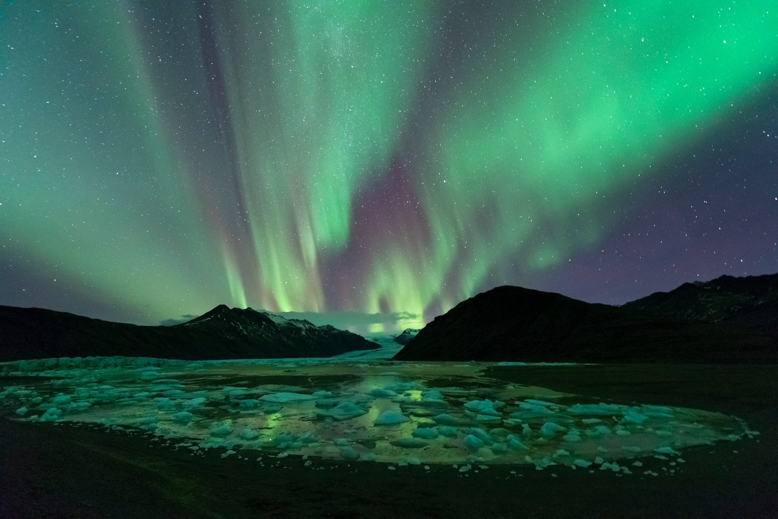 Northern lights above a glacier lagoon and dark mountains in South Iceland