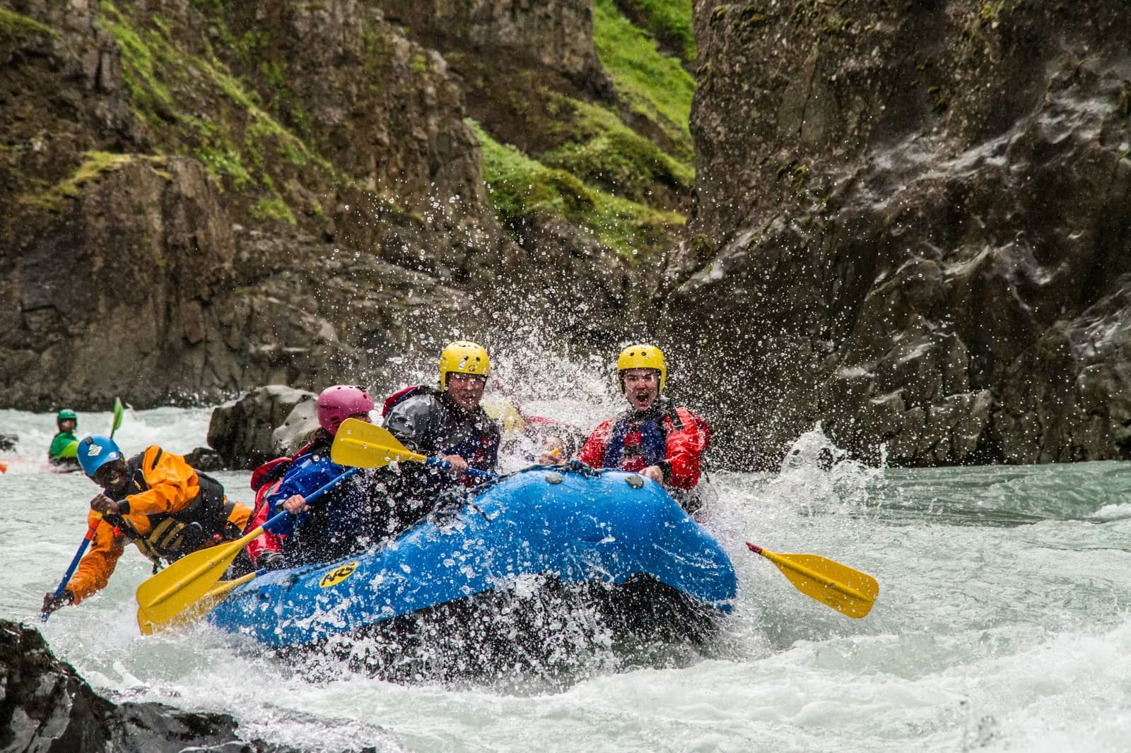 A guided raft team paddling together through a white-water rapid in Iceland.