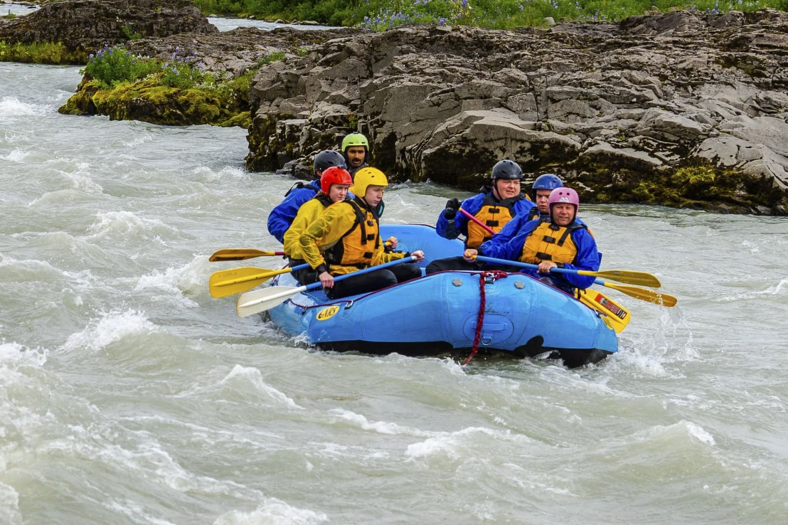 A guide and paddlers holding a blue raft on line through a rocky Hvítá rapid.