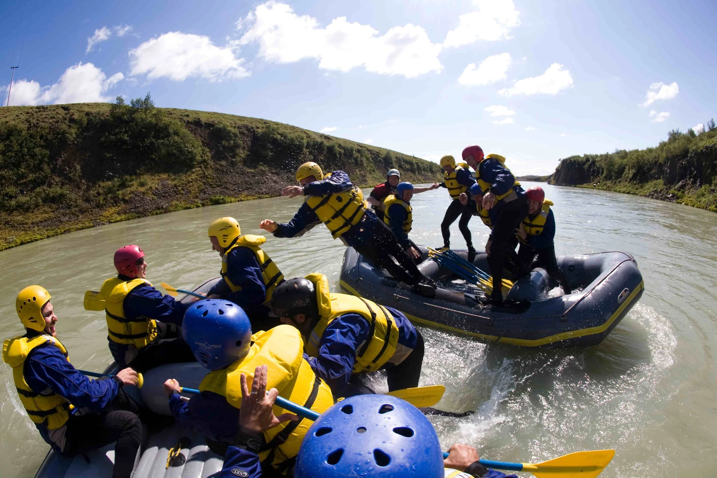 A rafting group in helmets and river suits practicing balance together on calmer water.