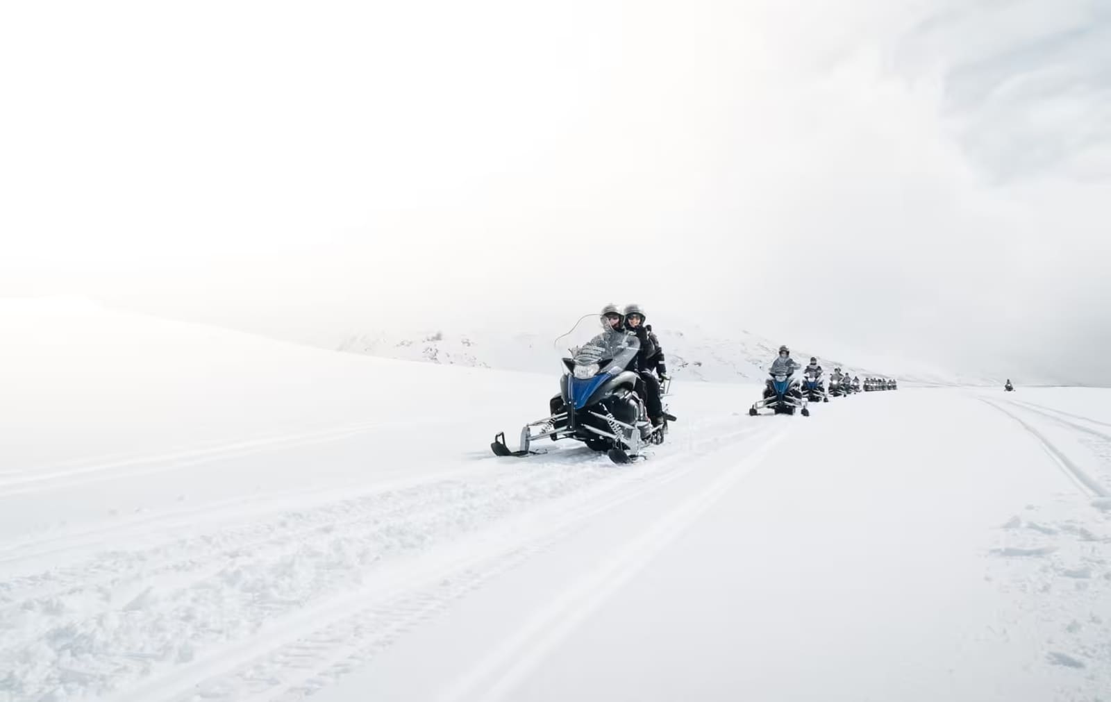A guided line of snowmobiles crossing a pale glacier in Iceland