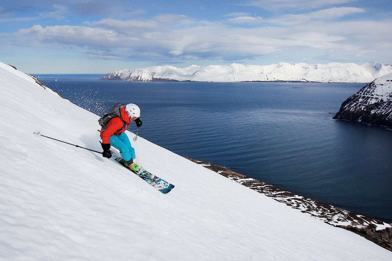 Skier descending a snowy Tröllaskagi slope above a dark North Iceland fjord