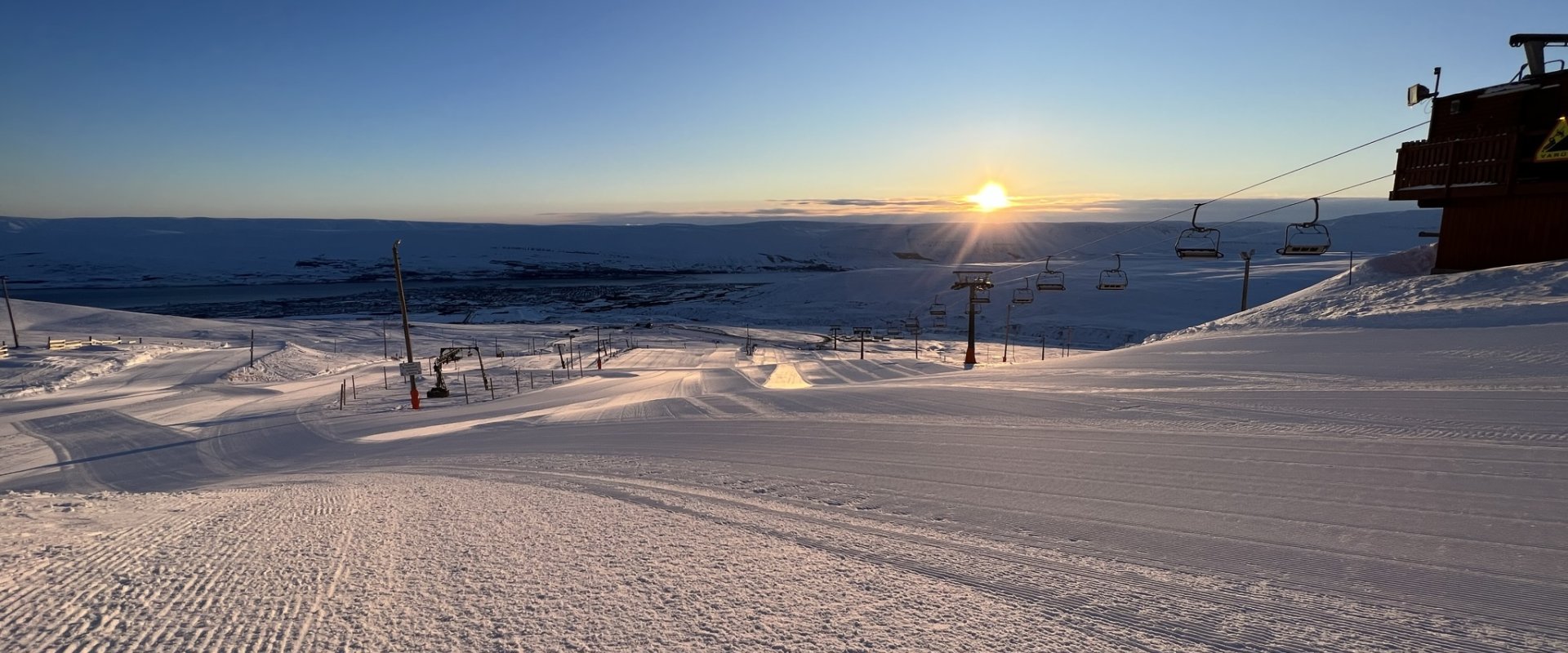 Groomed Hlíðarfjall piste and chairlifts above Akureyri under low winter sun
