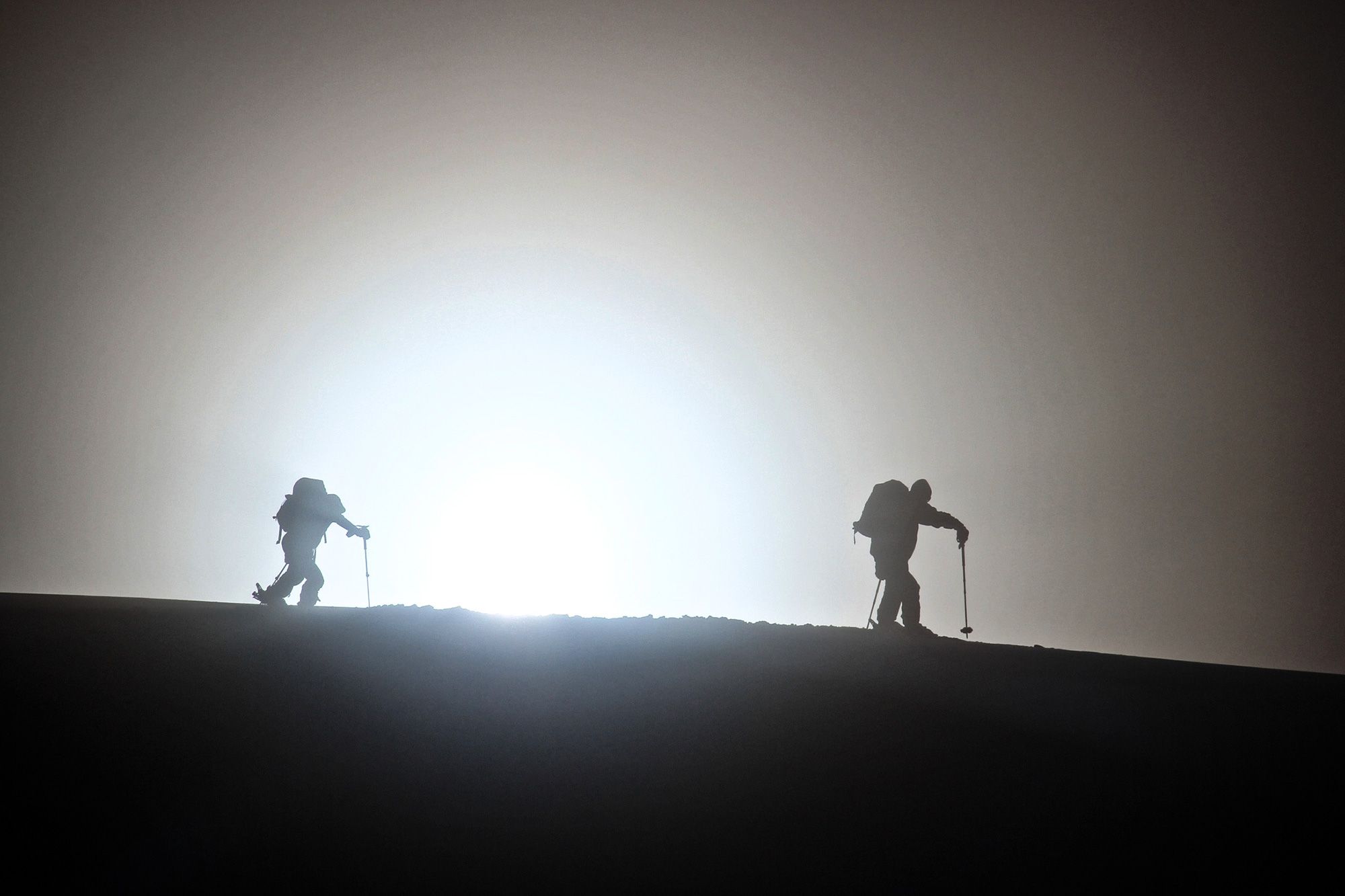 Two ski tourers climbing a snowy ridge in silhouette in North Iceland