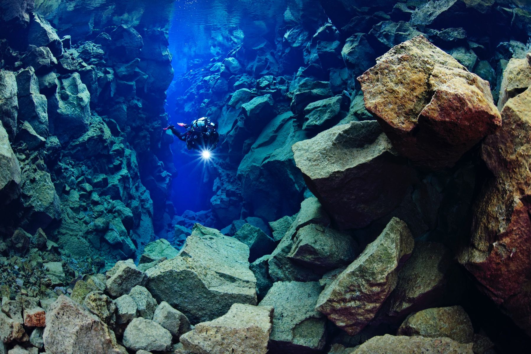 Scuba diver shining a light between rock walls in the Silfra canyon.