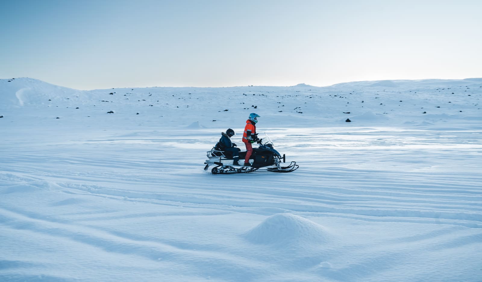 Travelers in winter riding gear snowmobiling on an Icelandic glacier