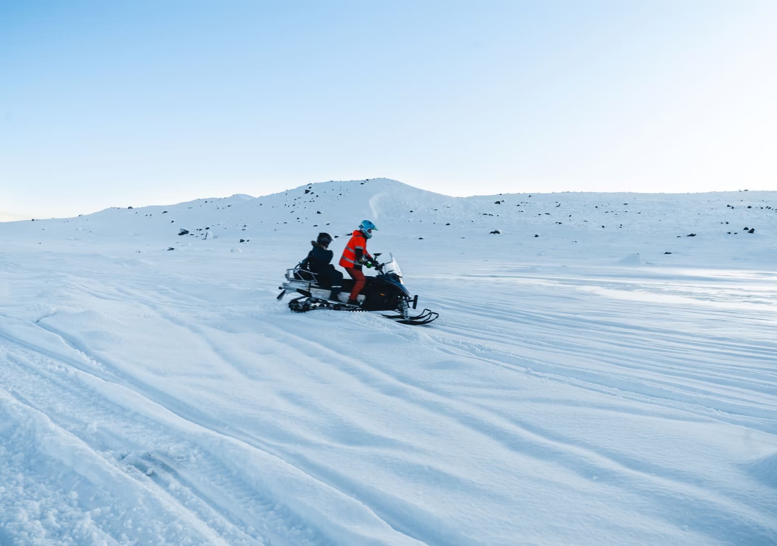 A driver and passenger riding one snowmobile across tracked snow in Iceland.