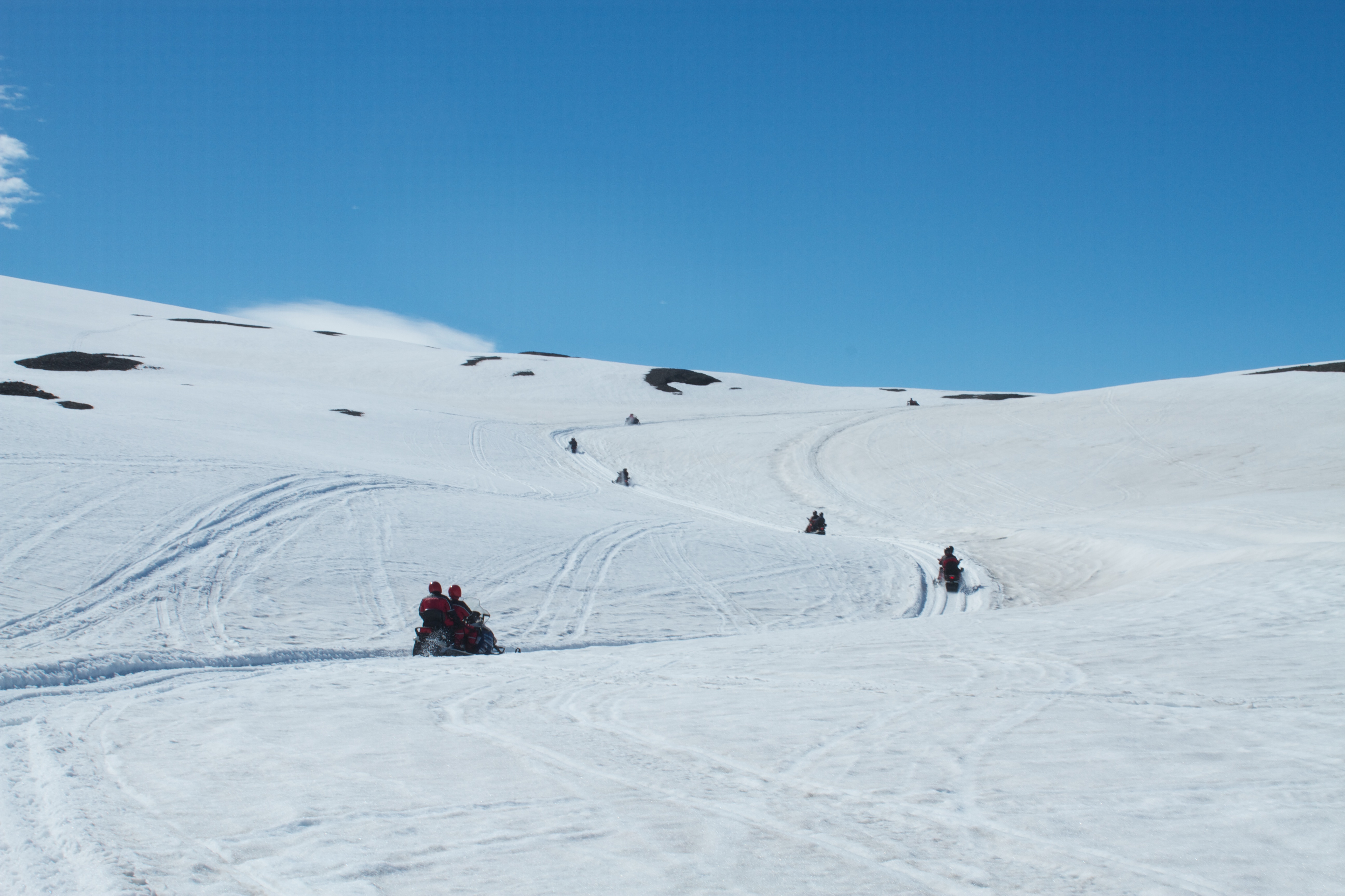 A guided group of snowmobilers following tracks over rolling snow on Vatnajökull.