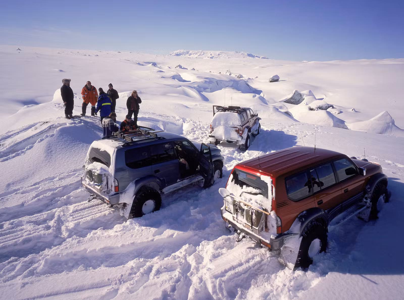 Travelers and three modified four-wheel-drive vehicles stopped in deep snow at Brúarjökull