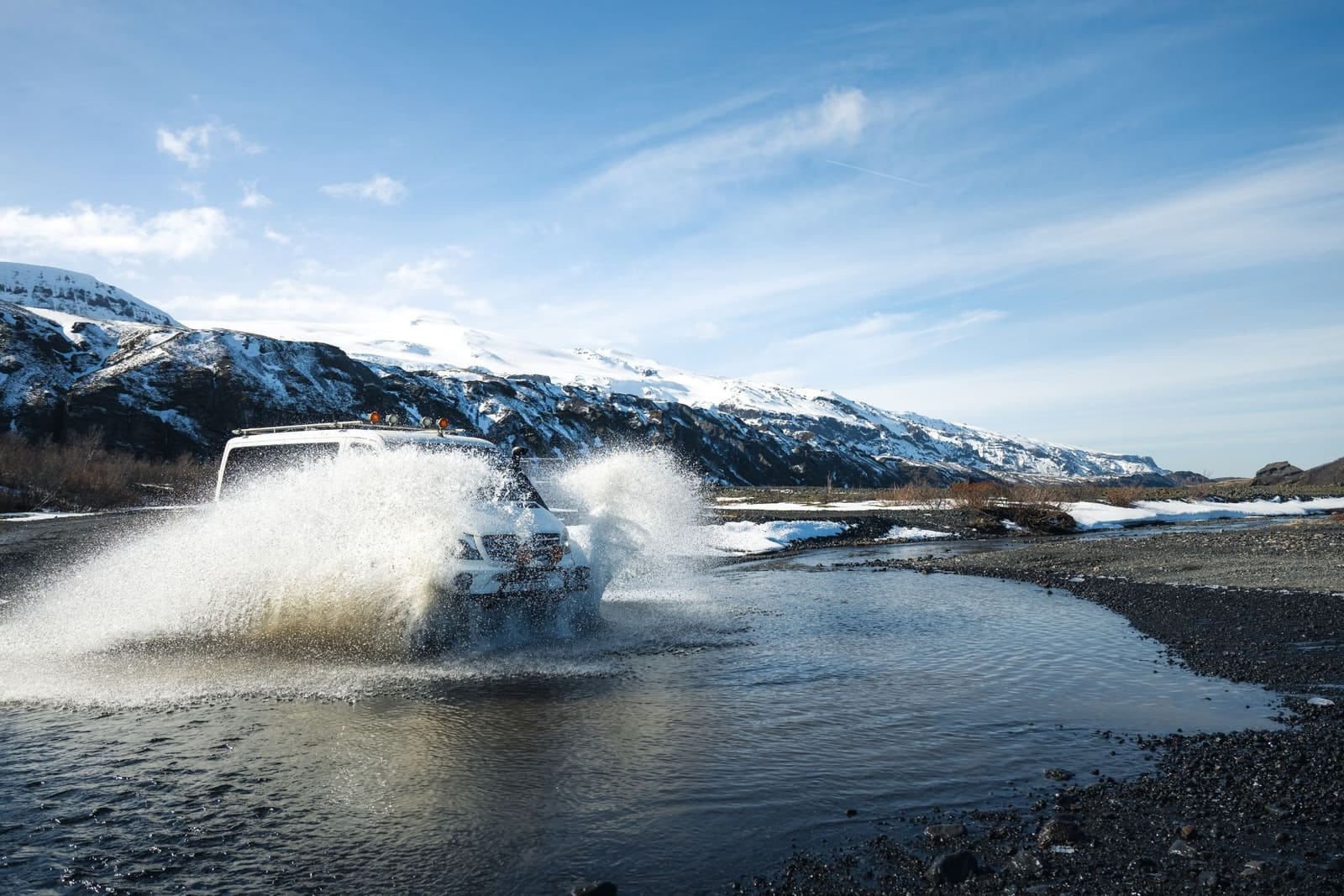Modified passenger vehicle splashing through a shallow winter river channel in Þórsmörk