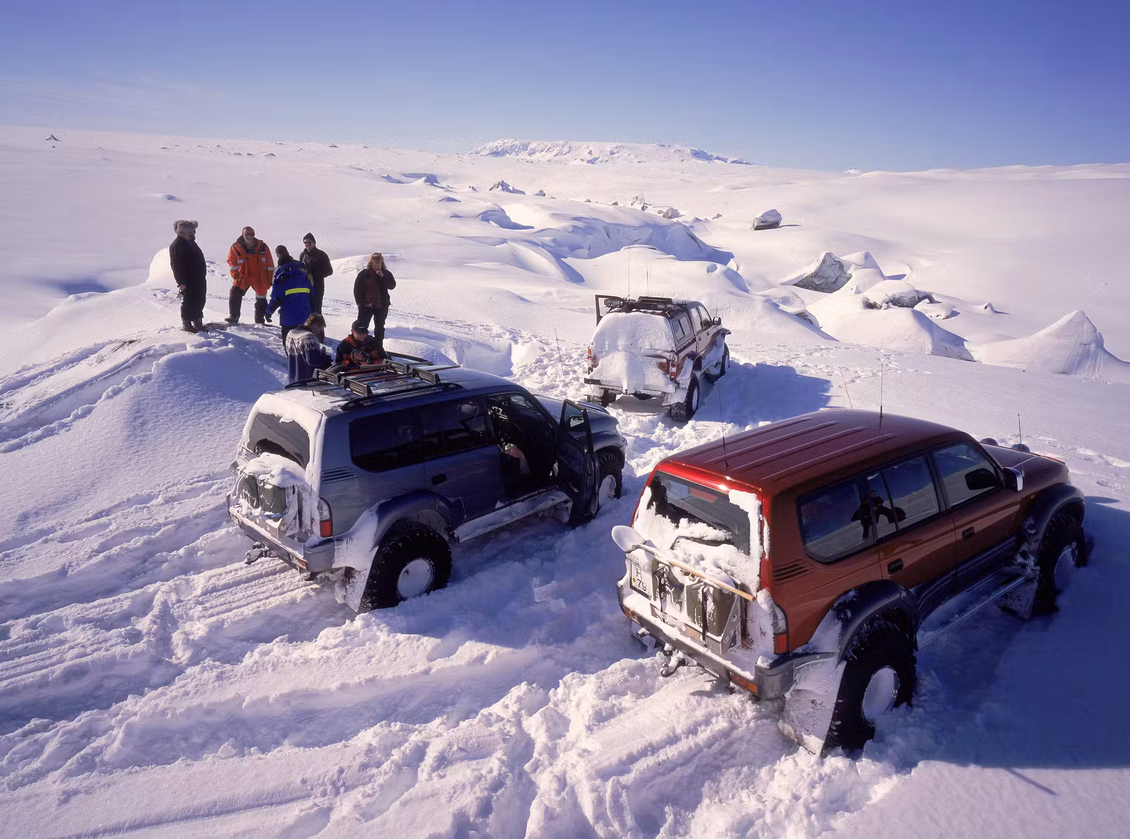 Travelers and three modified four-wheel-drive vehicles stopped in deep snow at Brúarjökull