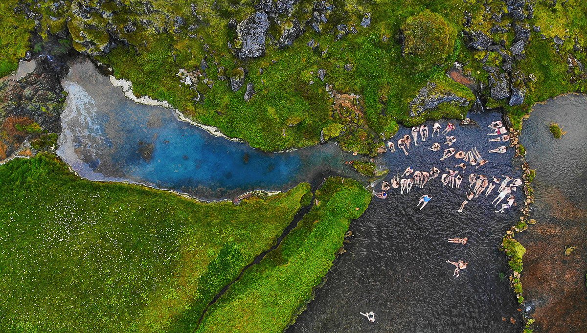 People soaking in the Landmannalaugar bathing brook beside green moss and dark water