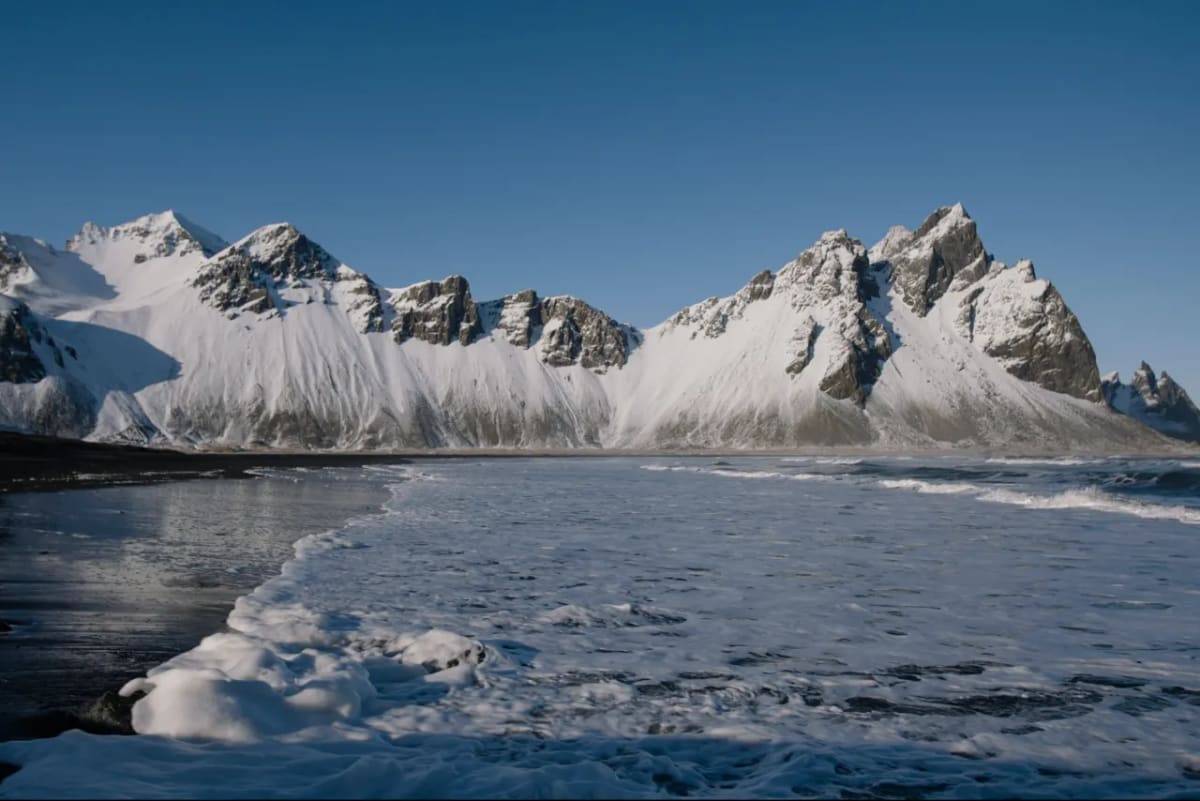 Snow-covered Vestrahorn above black sand and winter surf at Stokksnes