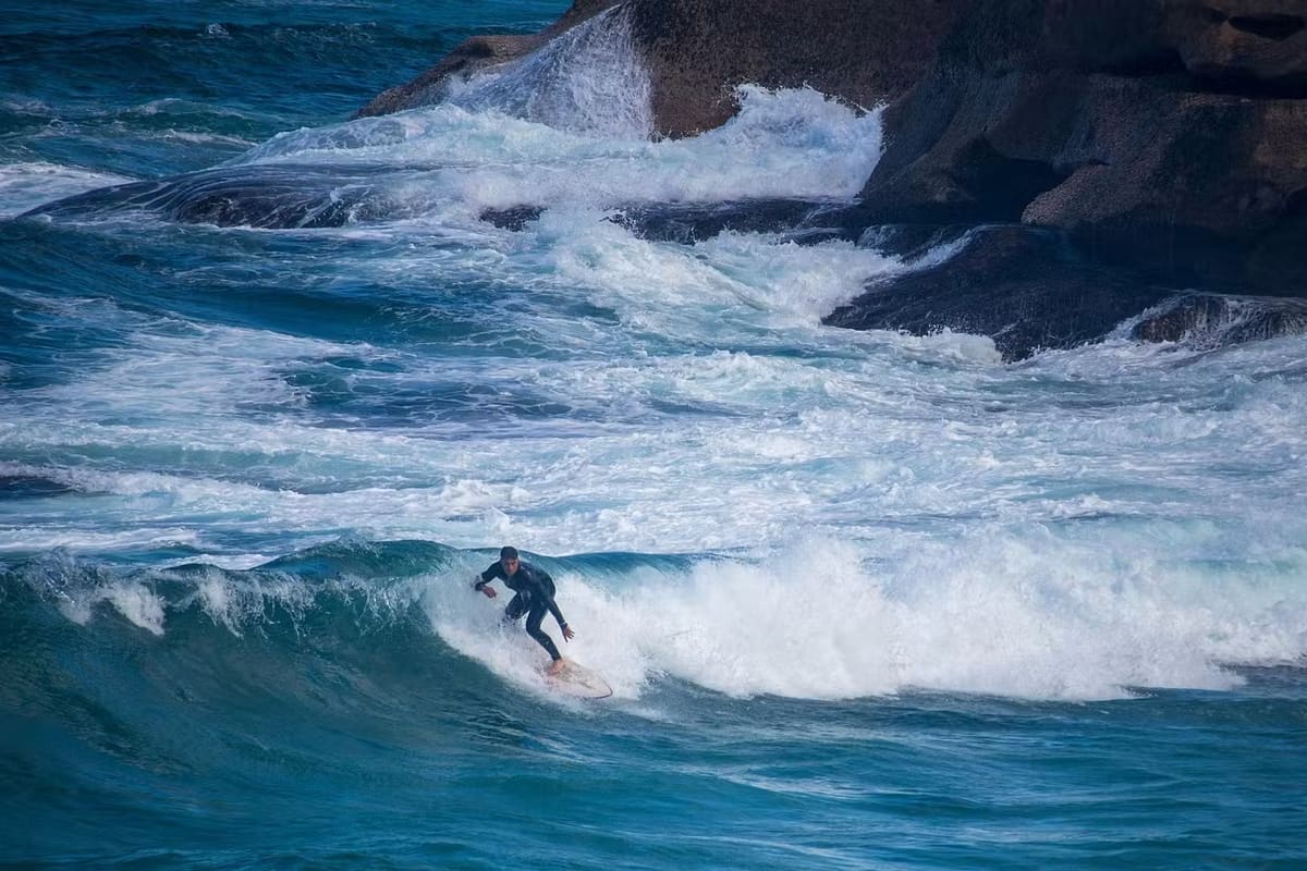 Surfer riding through white water near a dark rocky coast