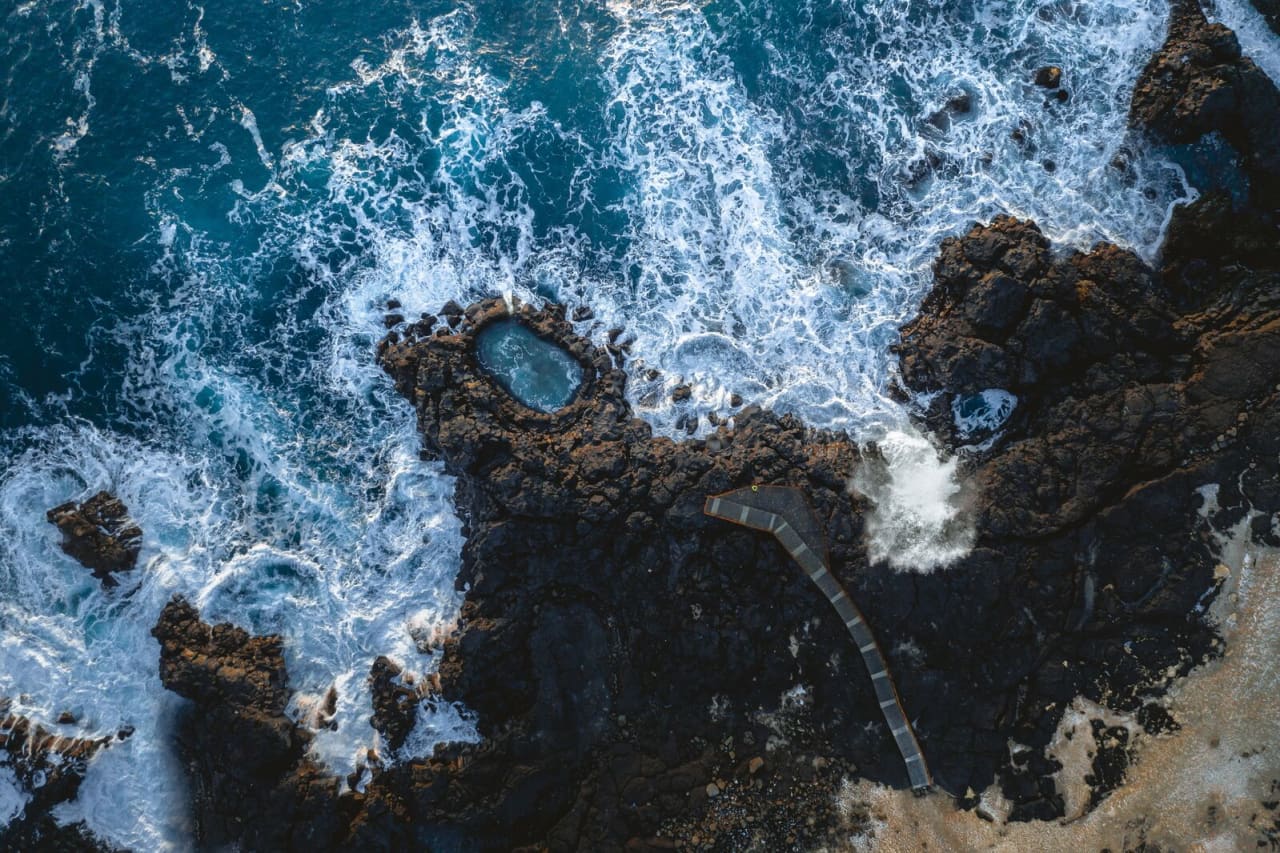Aerial view of waves surrounding Brimketill lava rocks and its viewing platform
