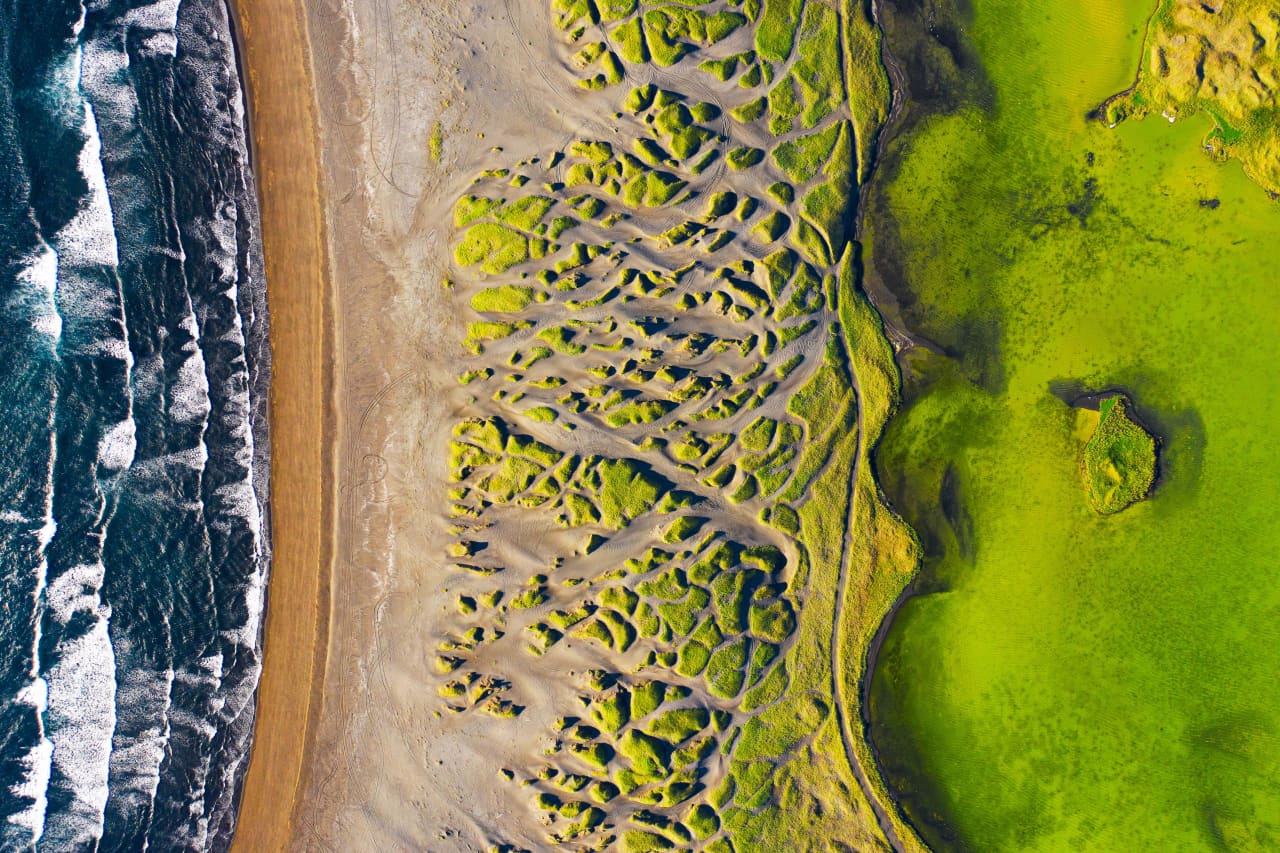 Aerial view of Stóra-Sandvík black beach, grassy dunes, pond, and Atlantic surf