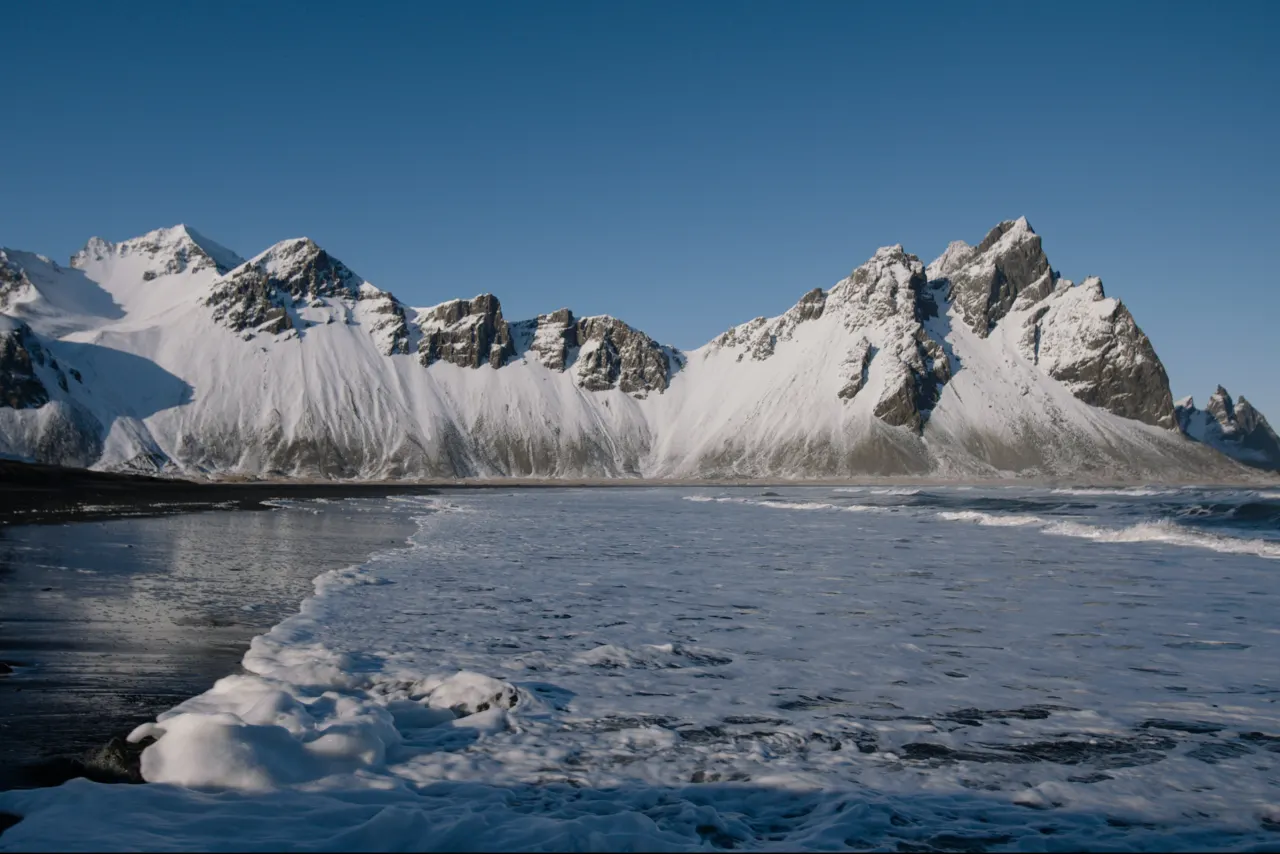 Snow-covered Vestrahorn above black sand and winter surf at Stokksnes