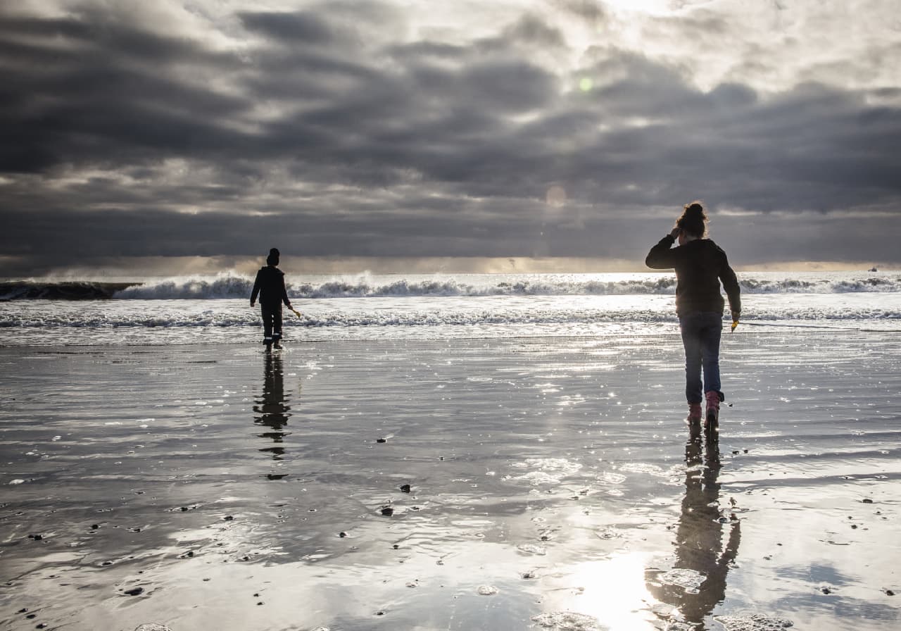 People walking on wet sand at Langisandur with low Atlantic surf offshore