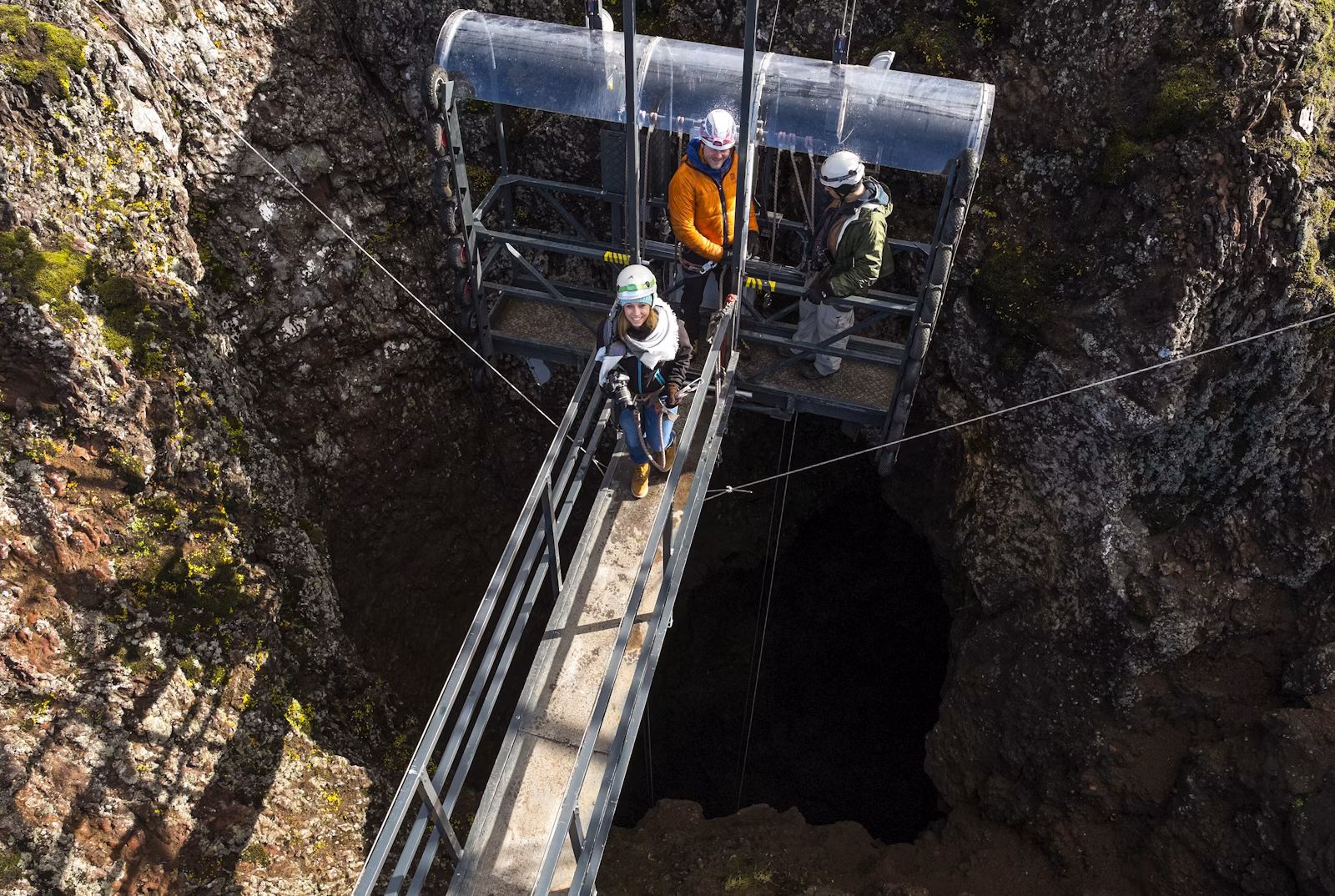 Helmeted visitors and a guide on the Þríhnúkagígur lift platform above the dark crater opening.