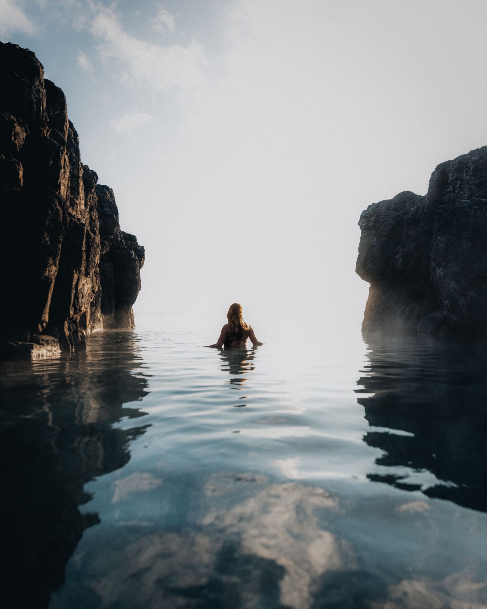 Single swimmer resting in warm water between dark rock walls at Sky Lagoon