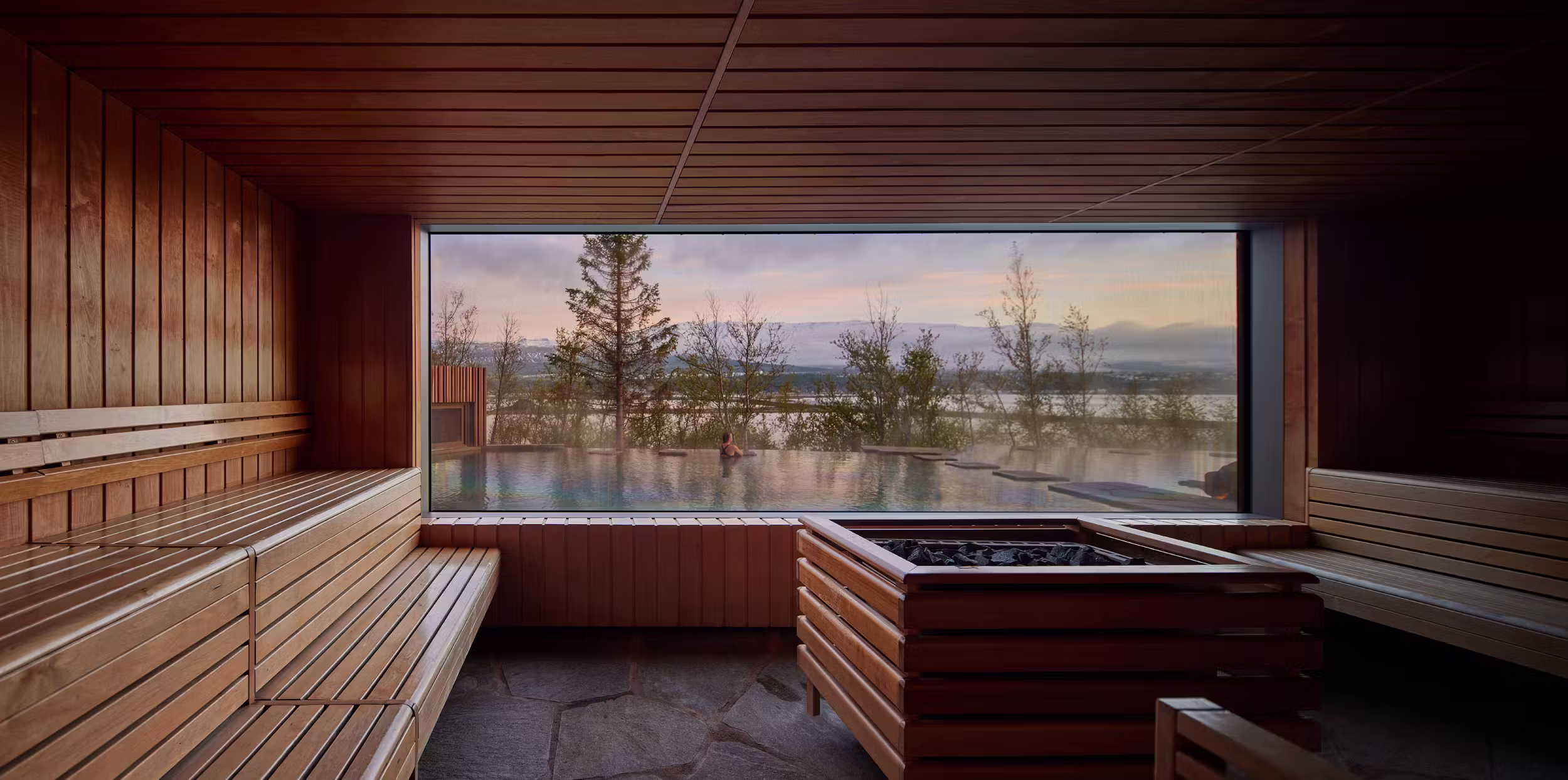 Wood sauna at Forest Lagoon with a wide window toward the pool, trees, and Eyjafjörður