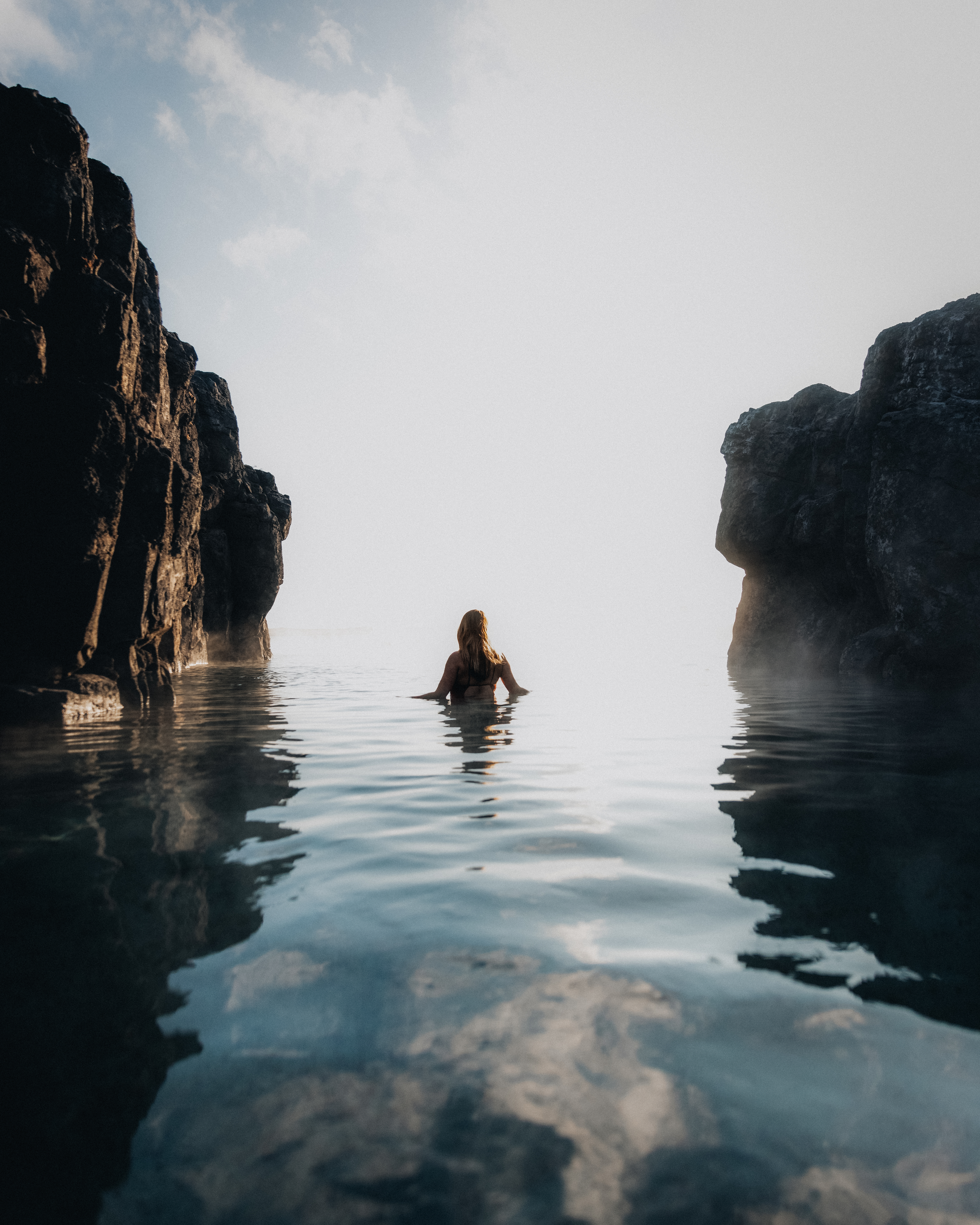 Single swimmer resting in warm water between dark rock walls at Sky Lagoon
