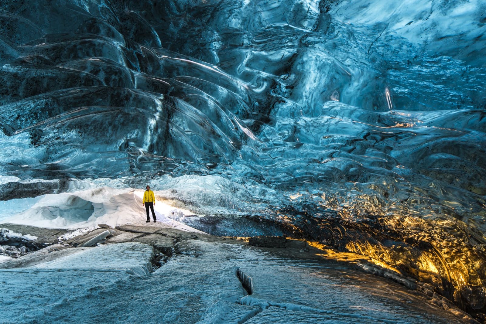 Person standing beneath blue ice inside a South Iceland ice cave.