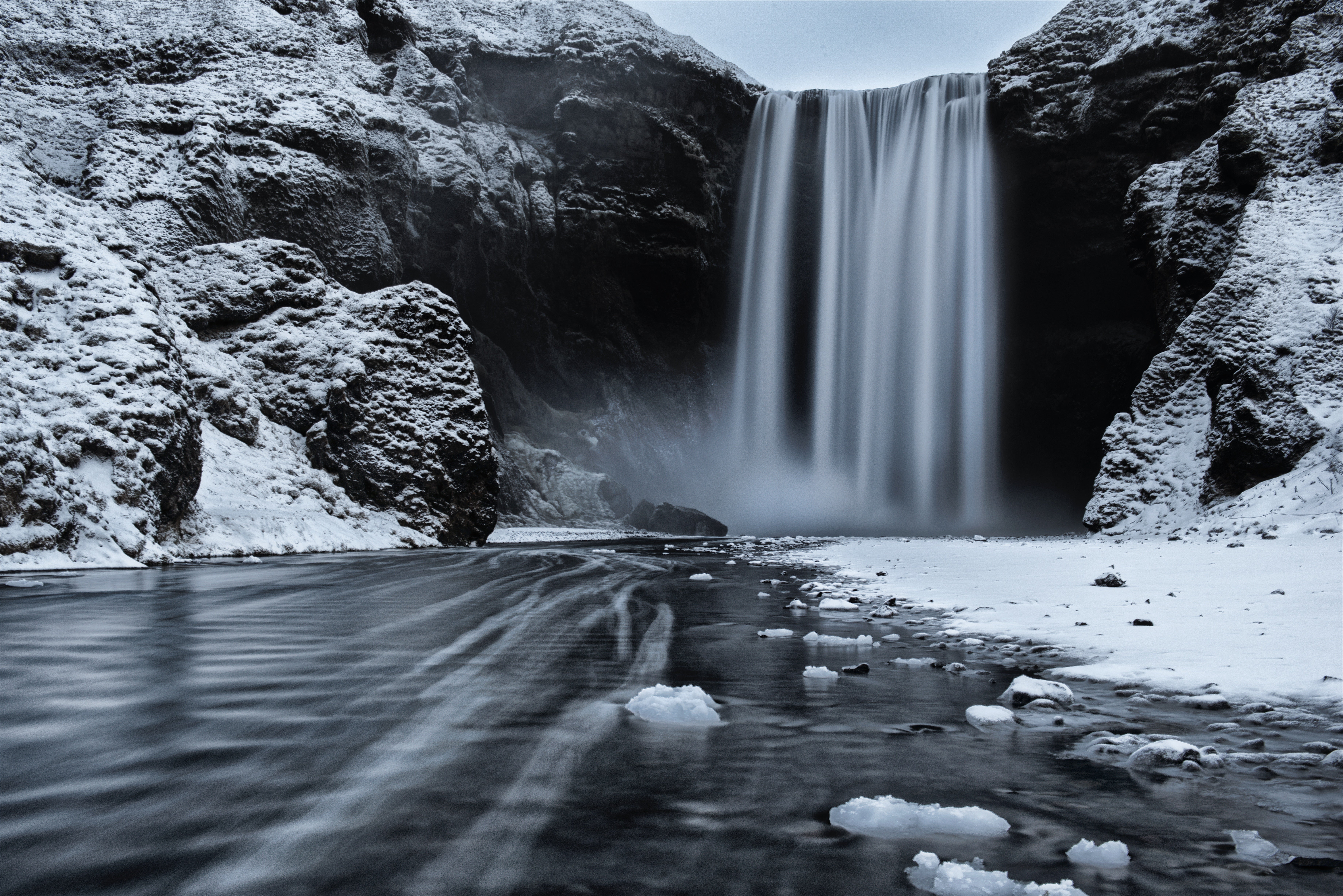 Snow-covered cliffs and icy water around Skogafoss in winter.