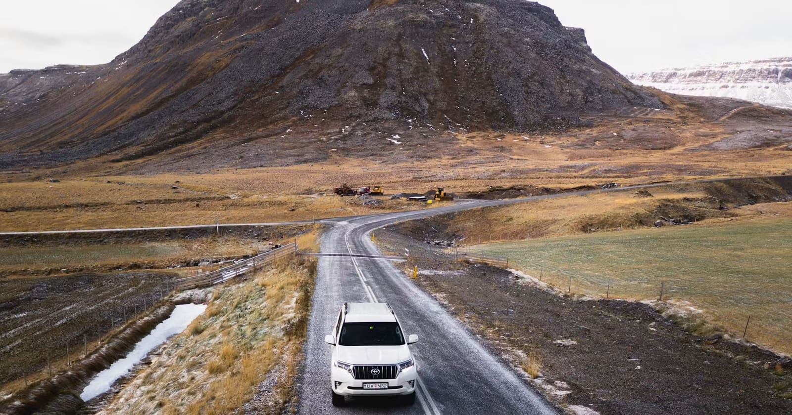 Vehicle driving a paved Iceland road through cold-season rocky terrain