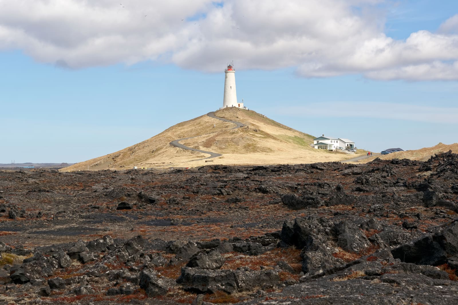 Reykjanes Lighthouse above a lava field under broken coastal cloud