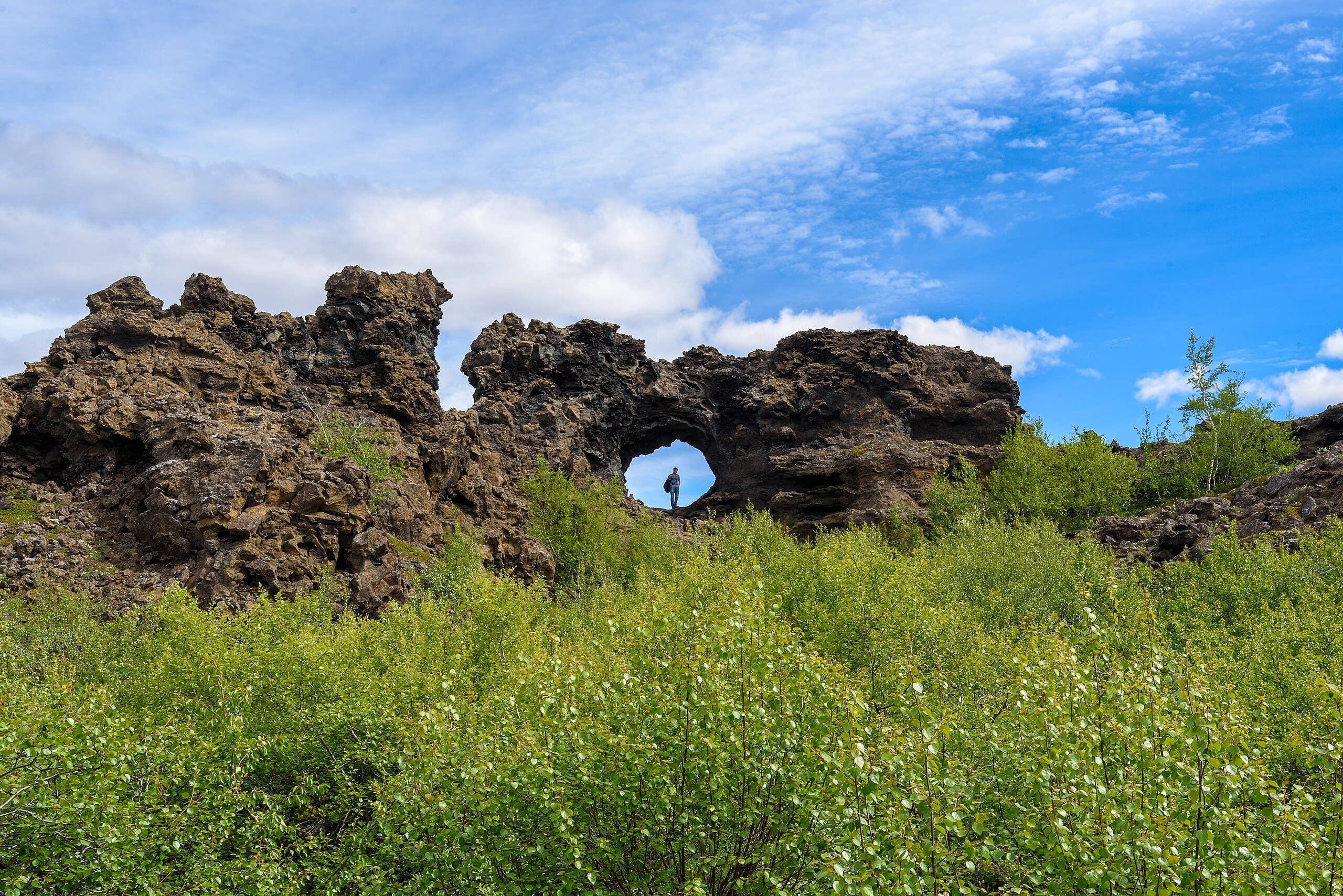 Marked walking path winding between dark Dimmuborgir lava towers and green summer vegetation.