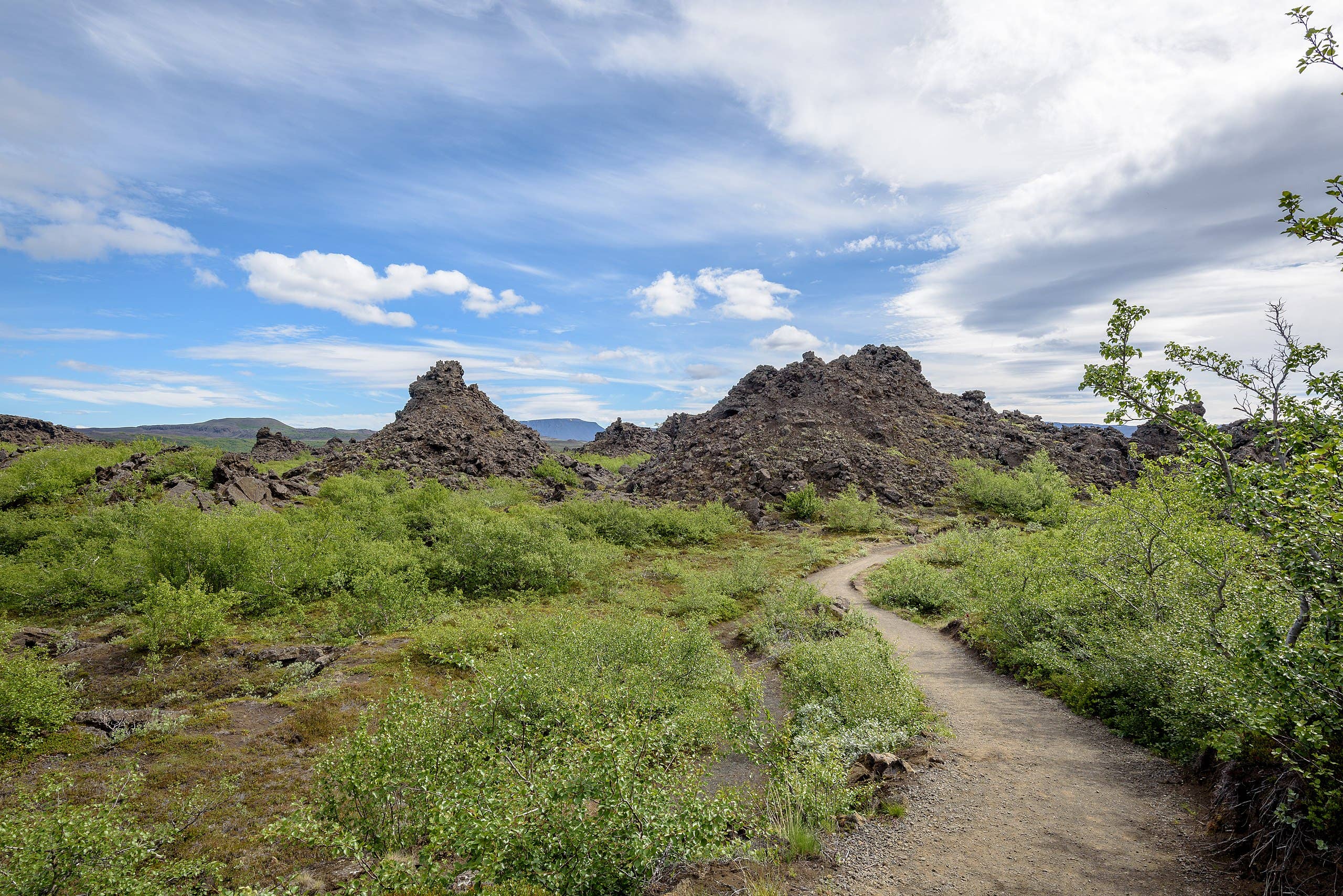 Wide Dimmuborgir lava wall with a natural arch and low vegetation below it.