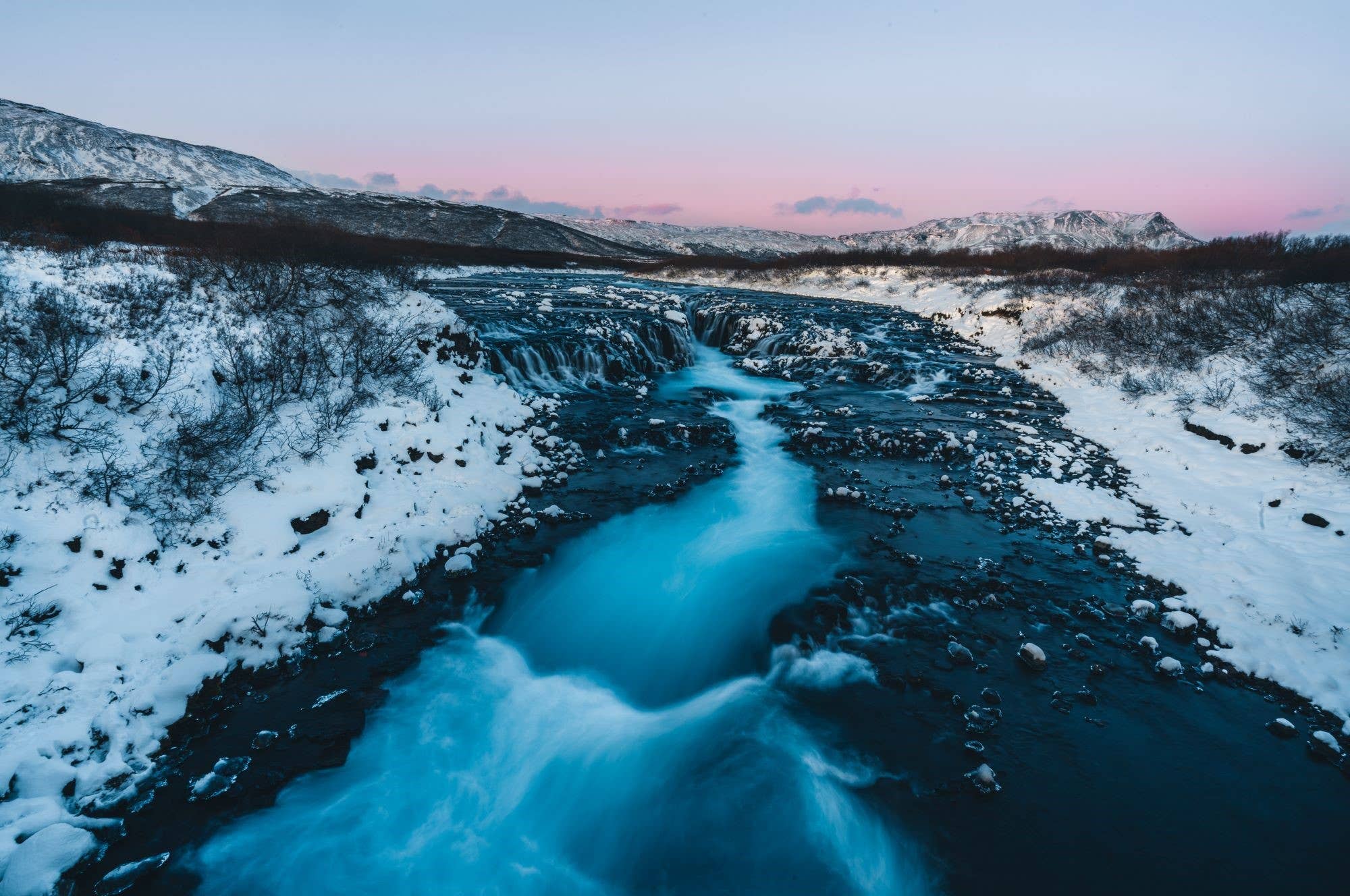 Brúarfoss Waterfall in winter with snow and ice around the blue river.
