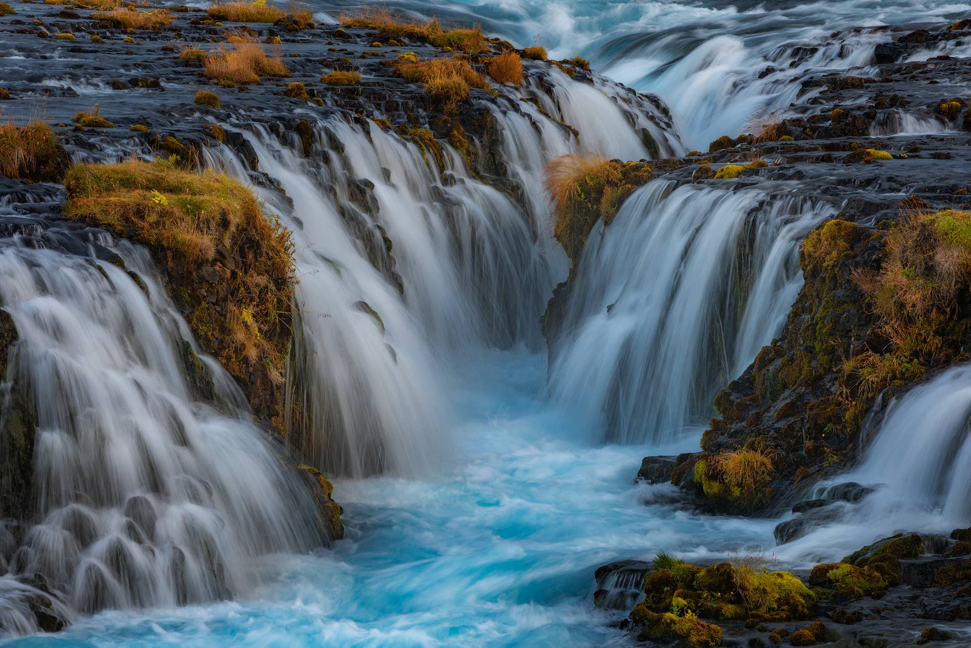 Close view of vivid blue water rushing through dark rock at Brúarfoss Waterfall.