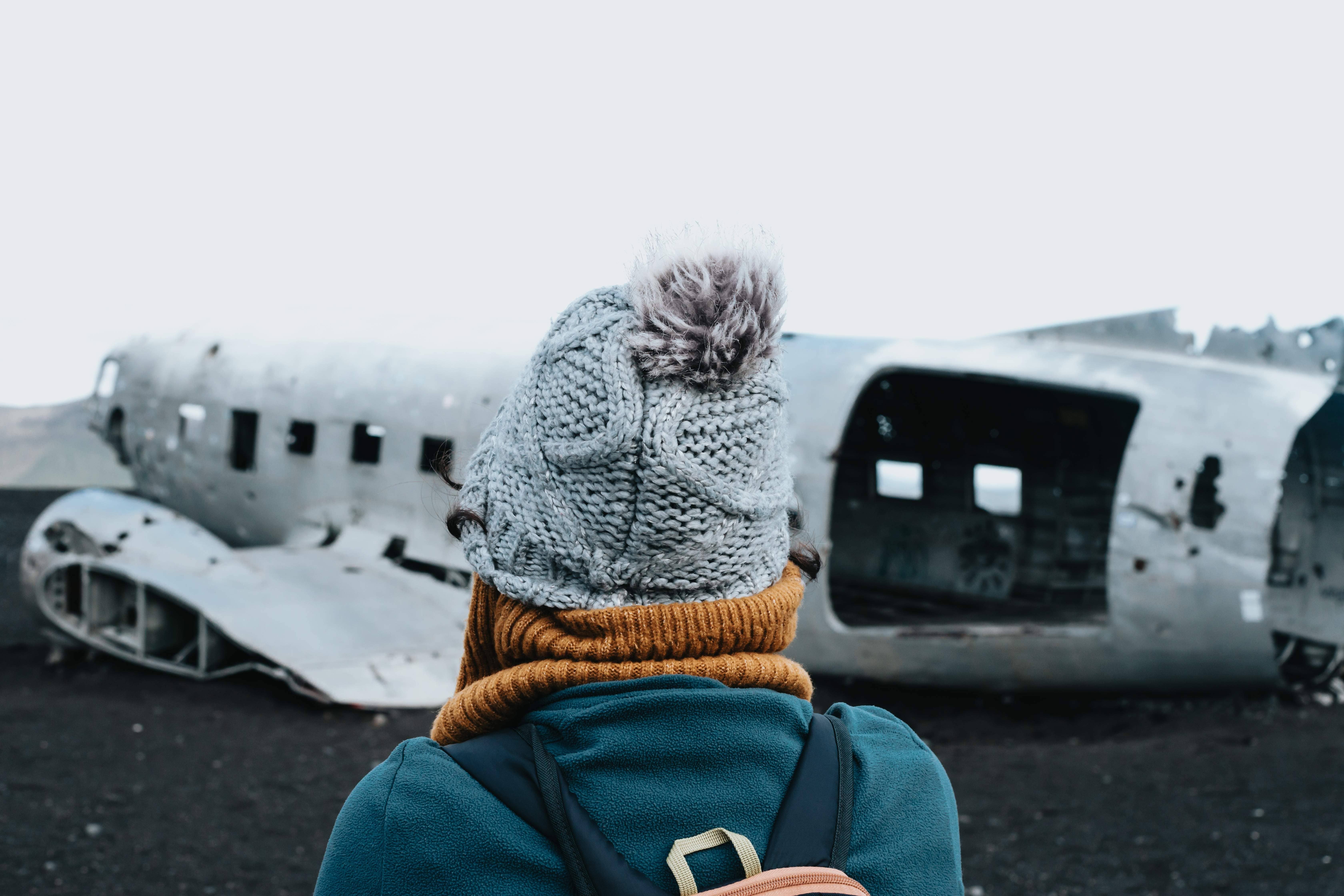 A visitor looking at the Sólheimasandur DC-3 Plane Wreck on a black sand plain.