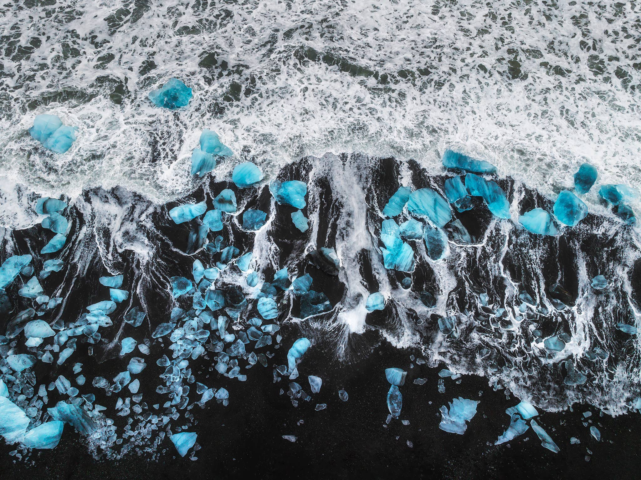 Aerial view of glacier ice scattered across the black sand at Diamond Beach.