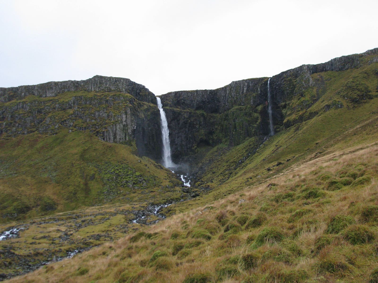Grundarfoss falling into a grassy basin below dark basalt cliffs near Grundarfjörður on Snæfellsnes.