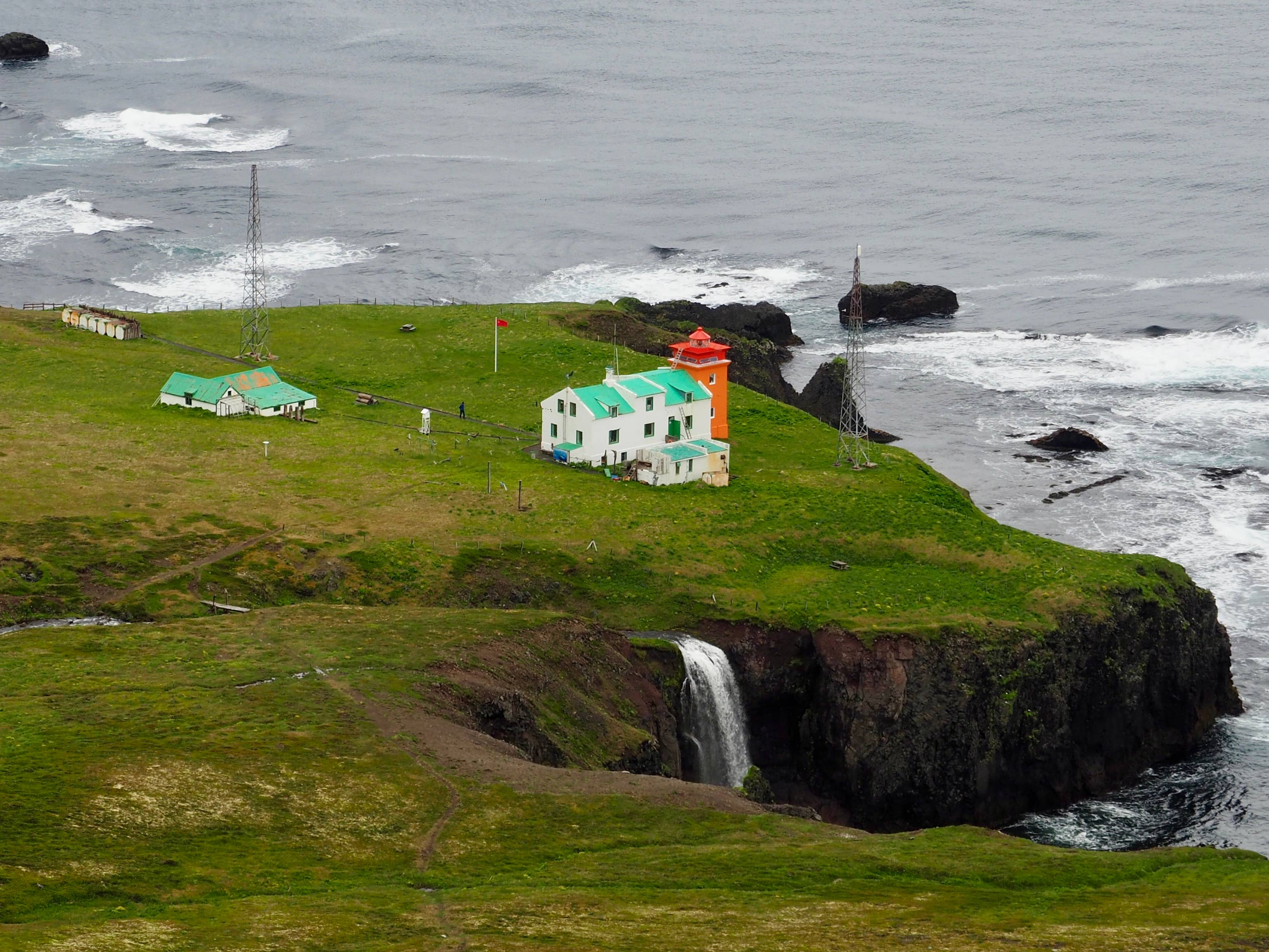 Hornbjarg lighthouse buildings on a grassy Hornstrandir cliff above waves.