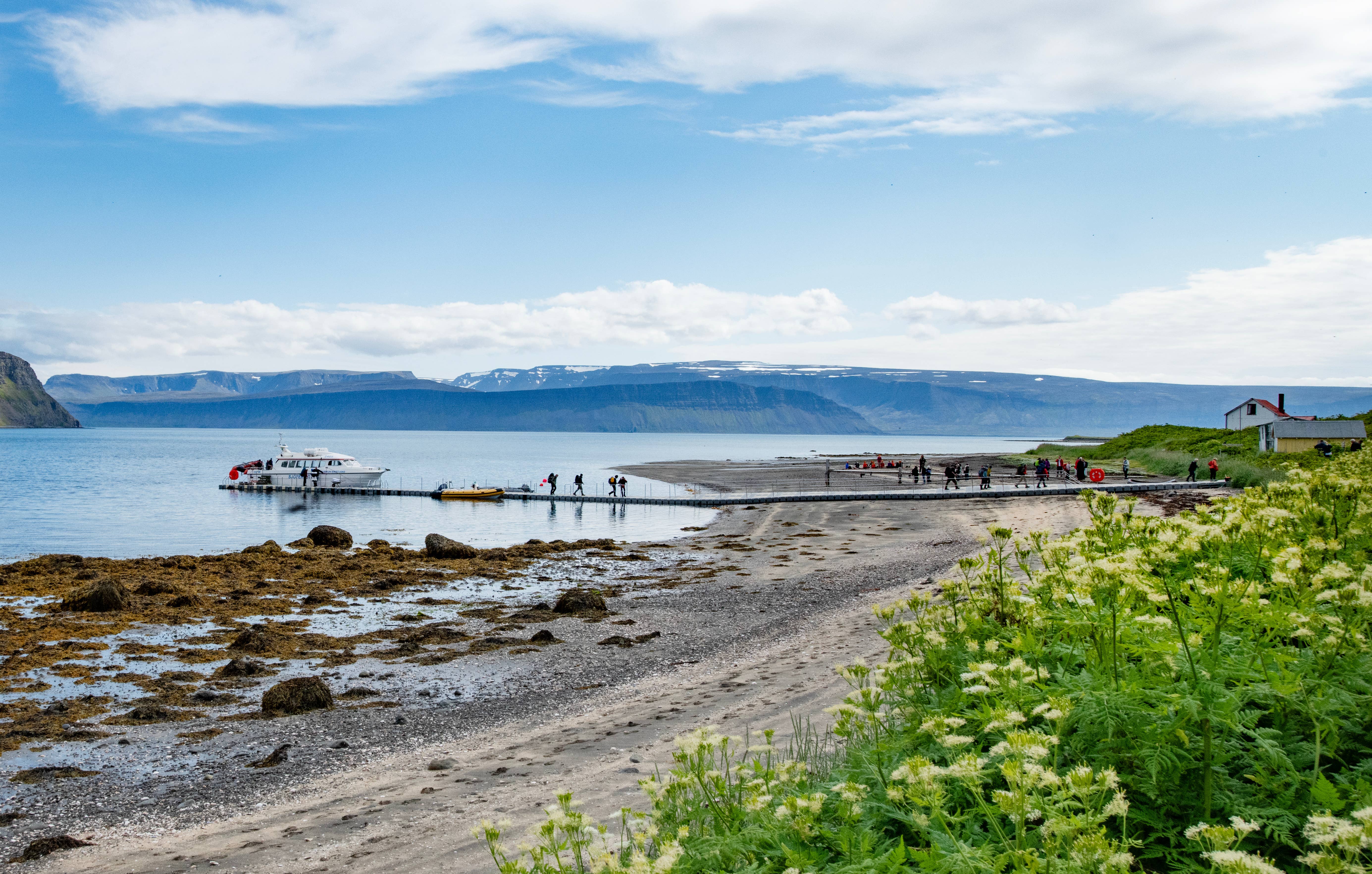 Boat landing at a Hornstrandir beach with hikers and fjord mountains behind.