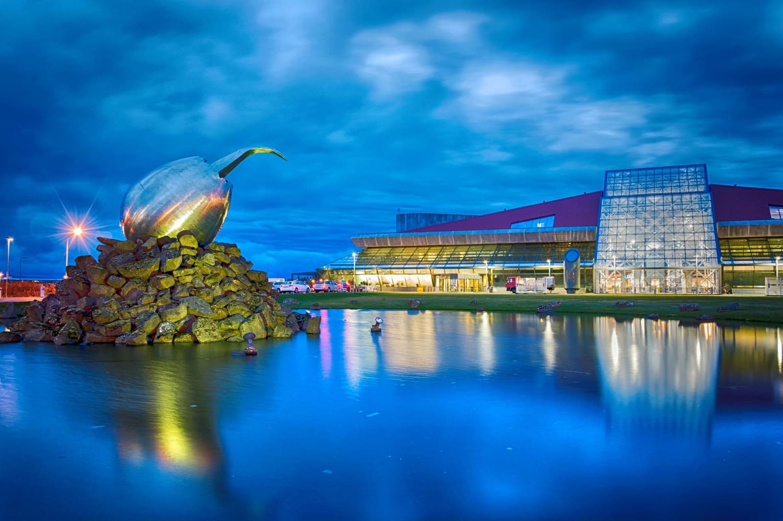 Keflavík International Airport terminal exterior and entrance sculpture at dusk.