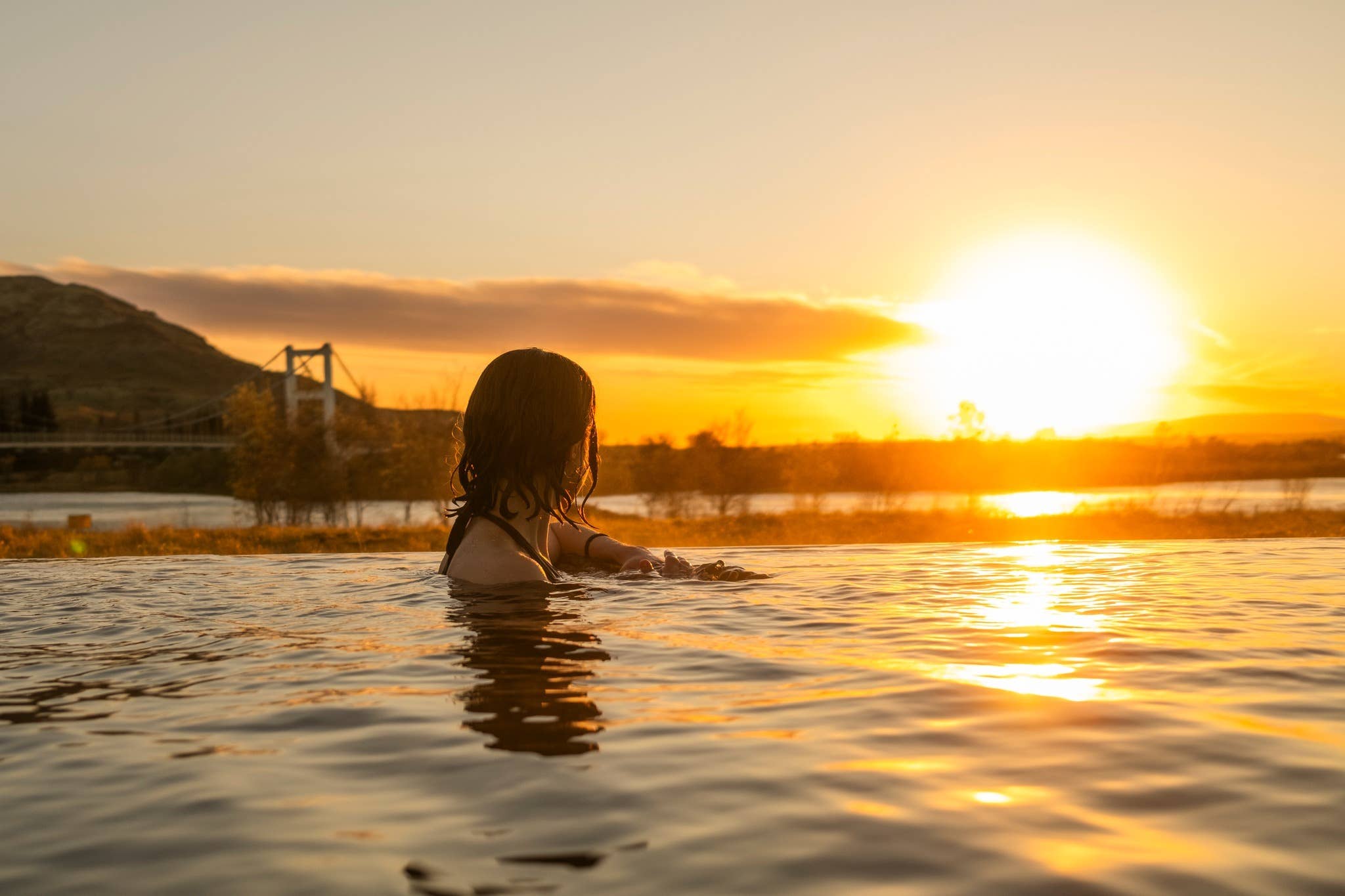Guests relaxing in Laugaras Lagoon with a bridge and mountains beyond the warm water.
