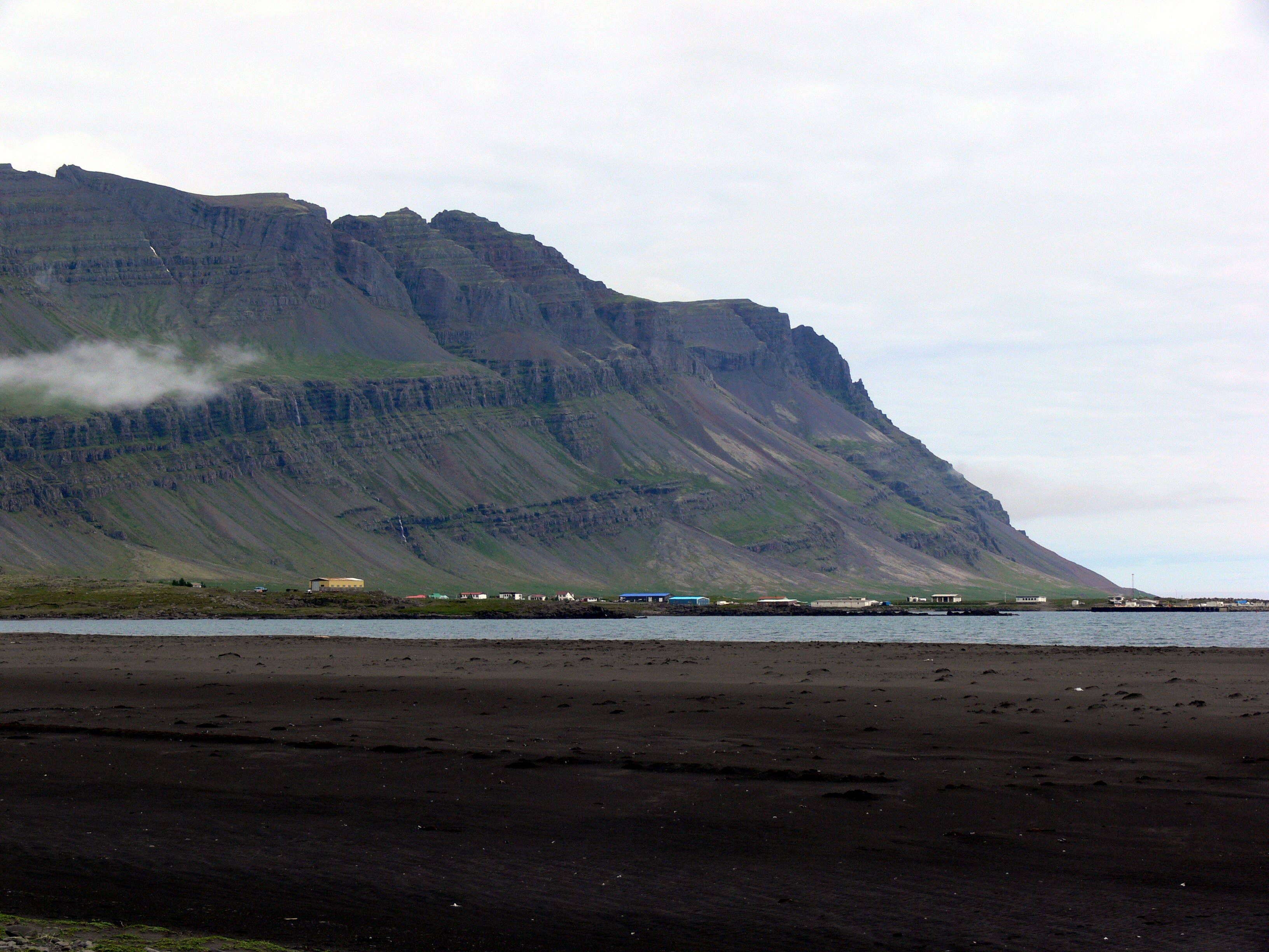 Black sand at Meleyri Beach with Breiðdalsvík and steep Eastfjords mountains across the bay.
