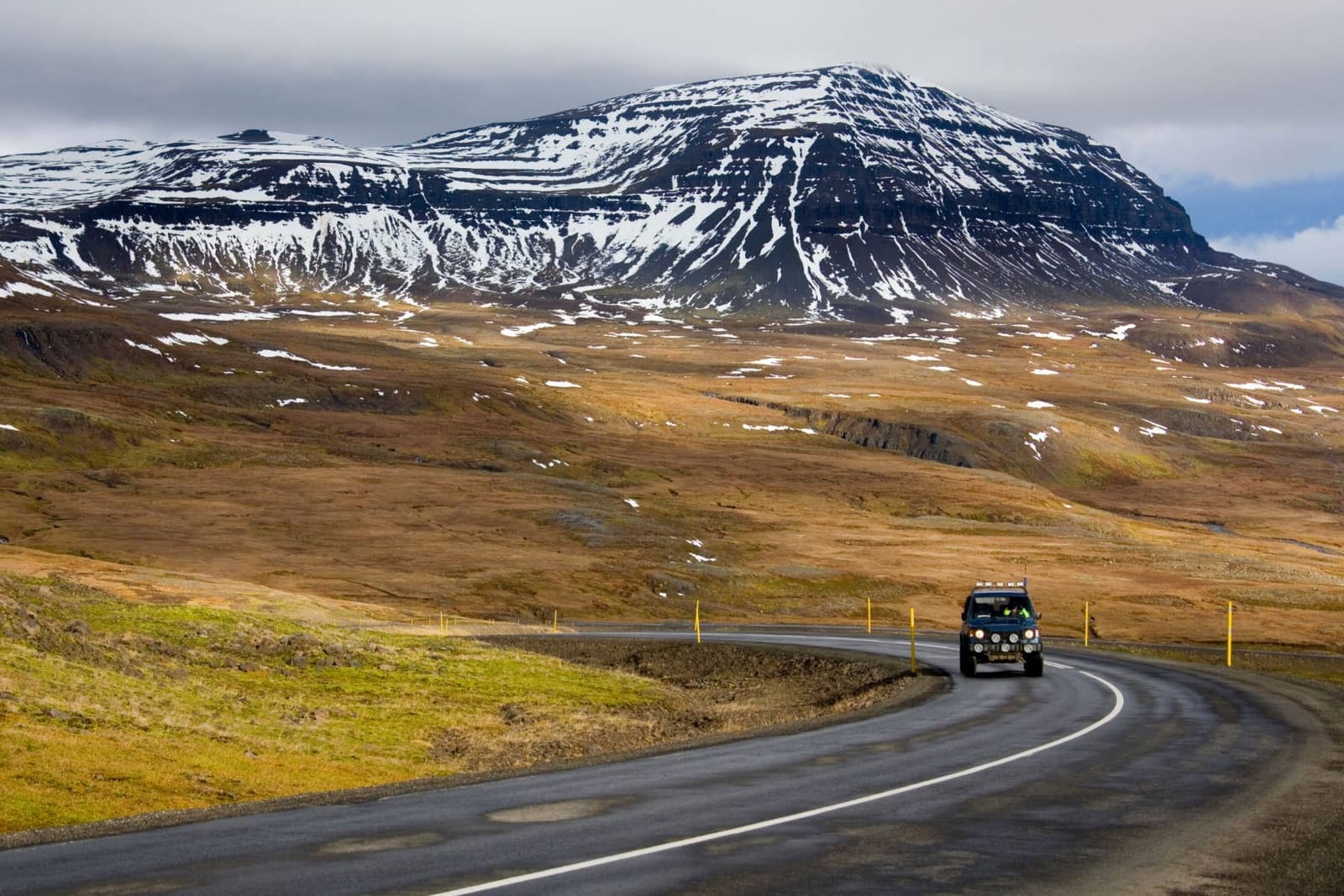 Car on Route 93 near Seyðisfjörður with open highland terrain and snow-streaked mountains.