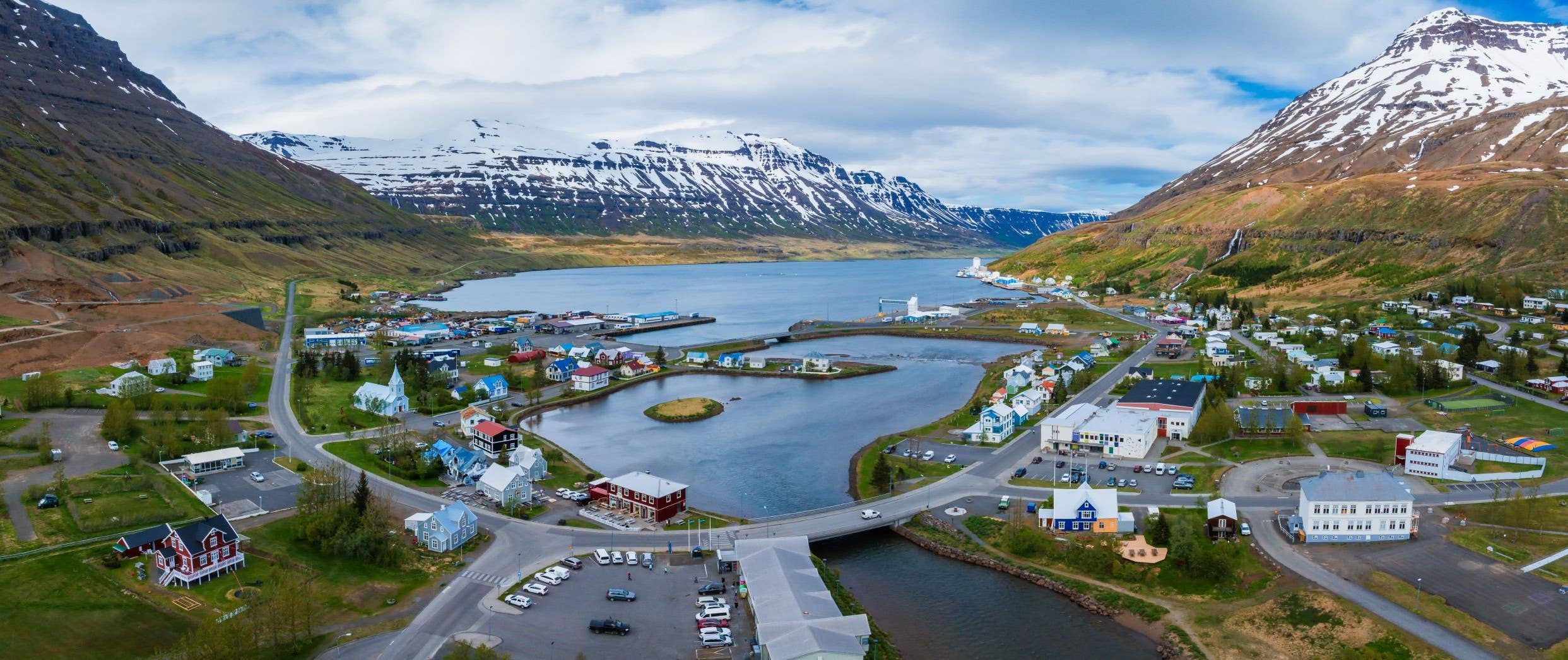 Aerial view of Seyðisfjörður fjord with town streets and steep mountains around the waterfall valleys.