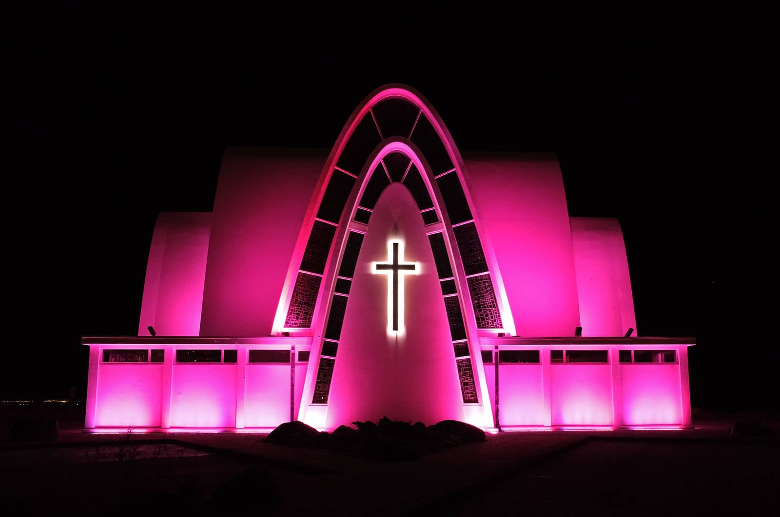 Kópavogskirkja Church lit at night with its arched facade glowing pink.