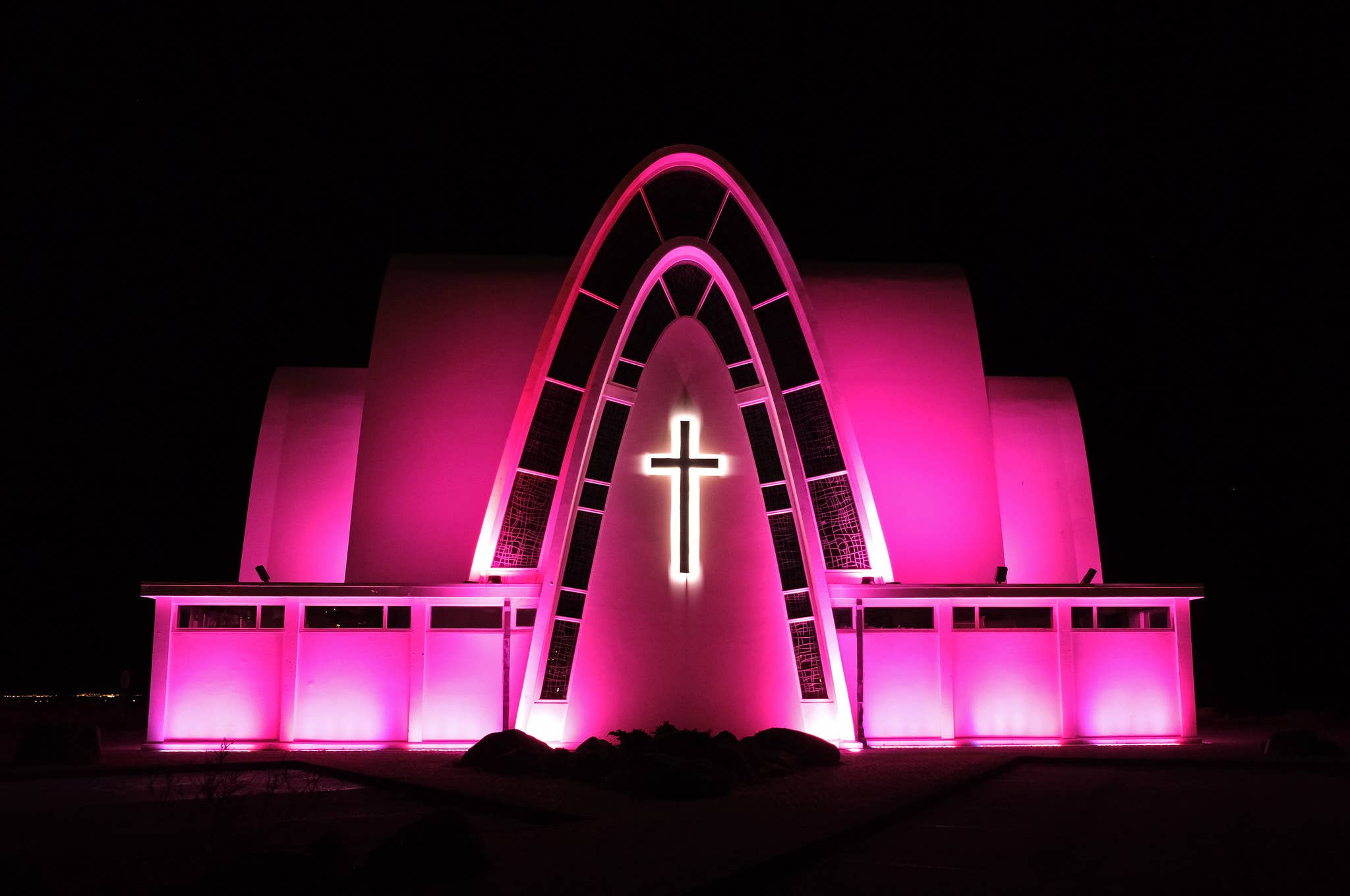 Kópavogskirkja Church lit at night with its arched facade glowing pink.